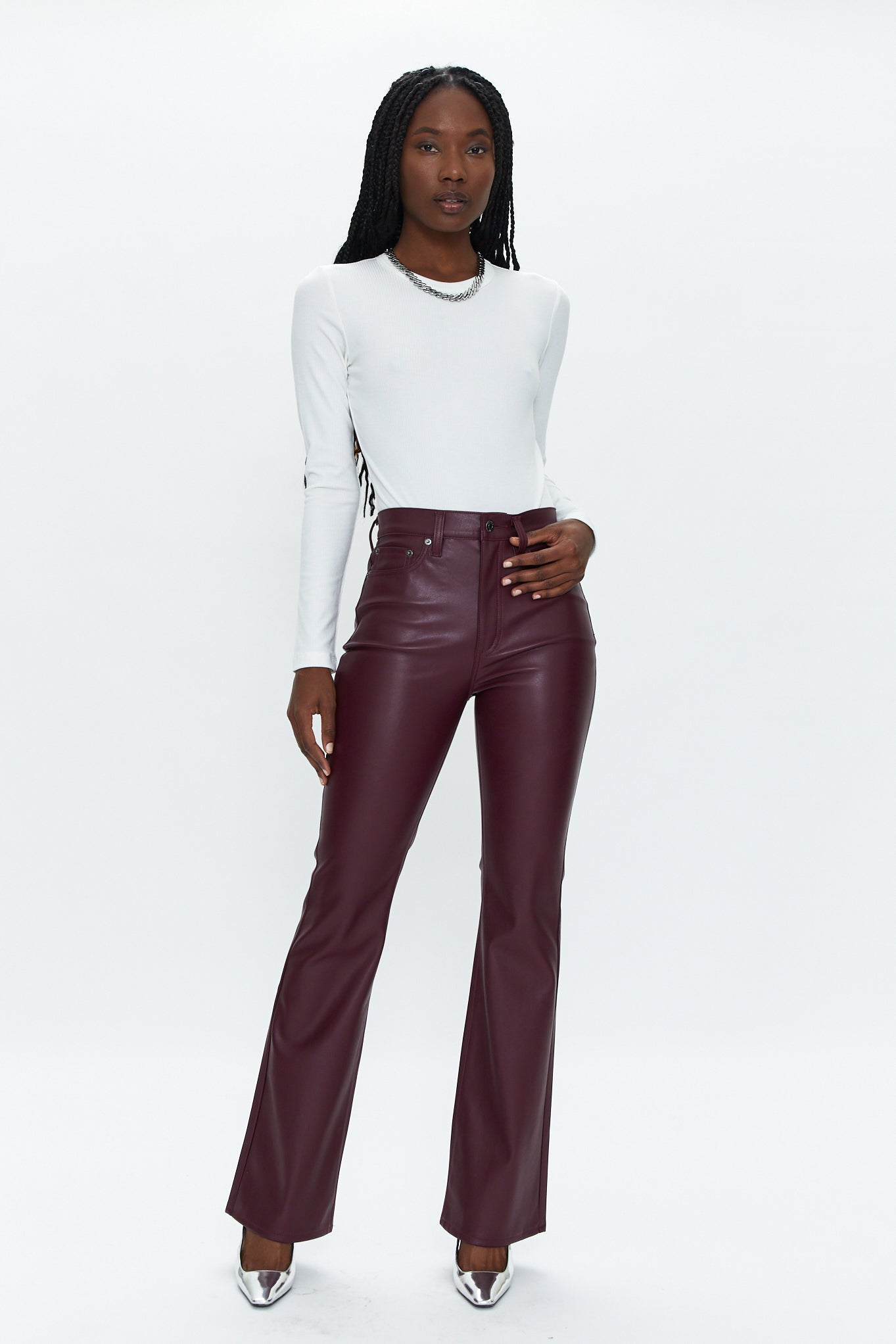 Woman wearing a white long-sleeve top and maroon leather pants on a white background