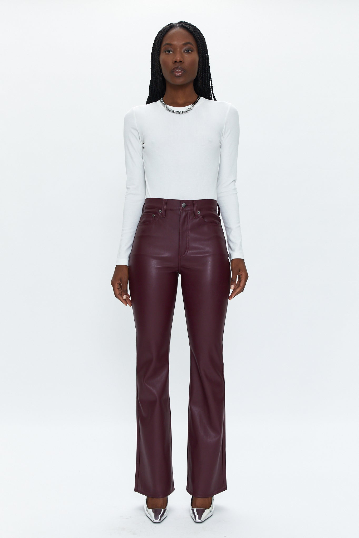 Person wearing a white long-sleeve top and burgundy leather pants on a white background