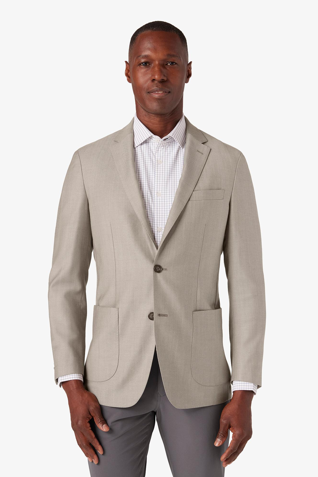 Man wearing a beige blazer over a white shirt with gray pants on a white background
