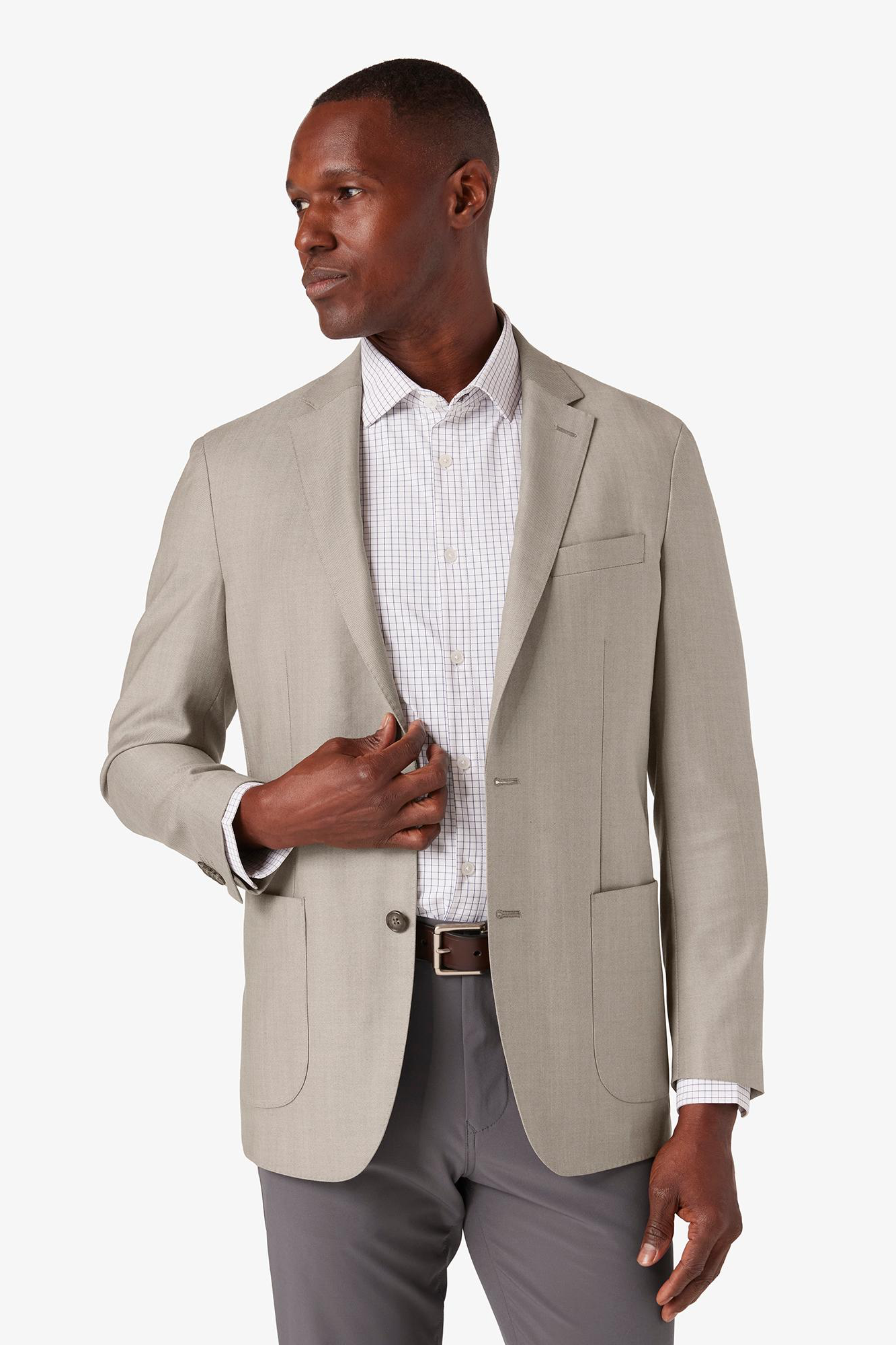 Man wearing a beige blazer over a white shirt with gray pants on a white background