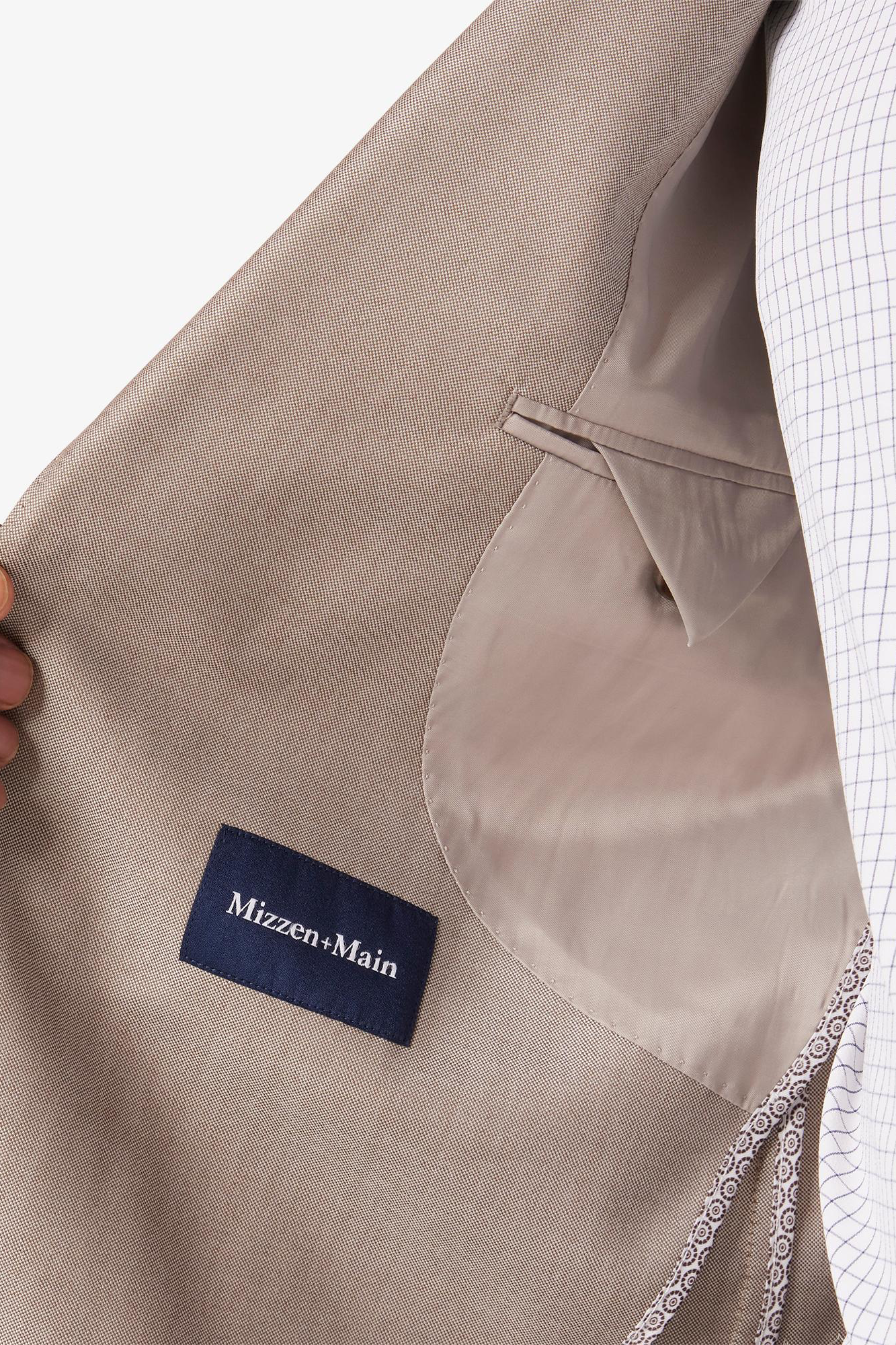 Close-up of a beige jacket with a Mizzen+Main label on a white background