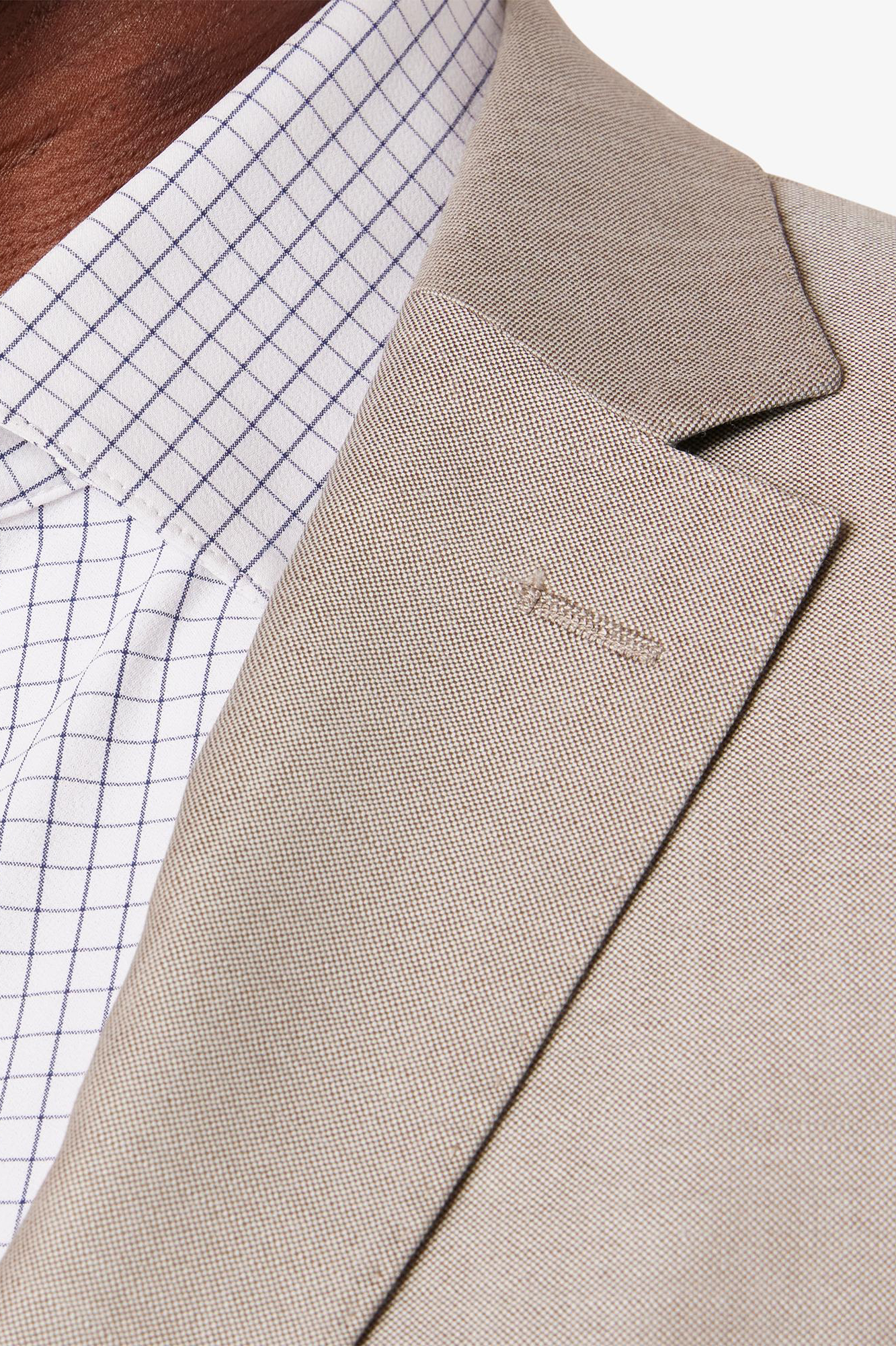 Close-up of a beige blazer with a brand logo on a white background