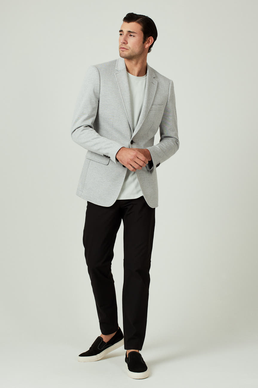 Man wearing a light gray blazer, white shirt, black pants, and black shoes on a white background