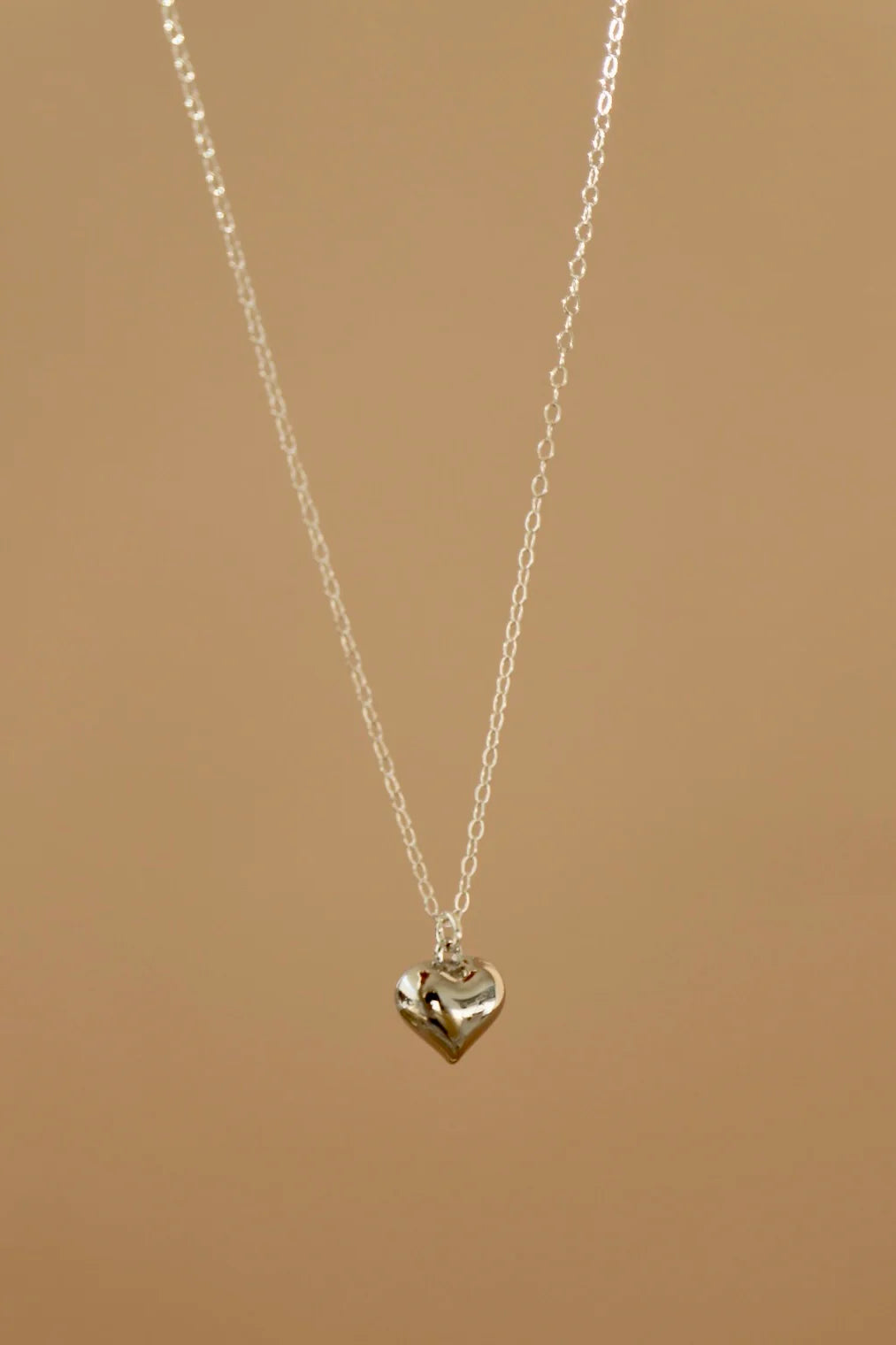 Silver heart-shaped pendant necklace on a beige background