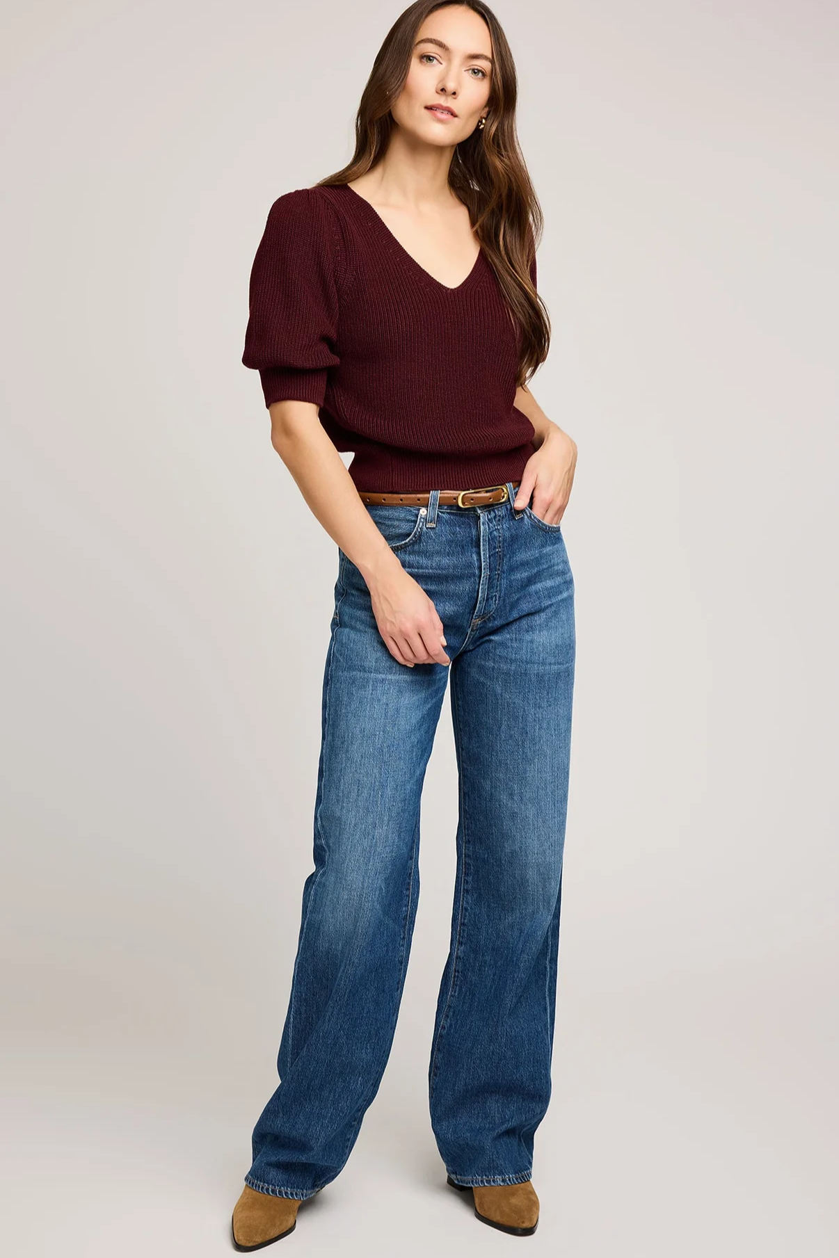 Woman wearing a burgundy top and blue jeans on a plain background
