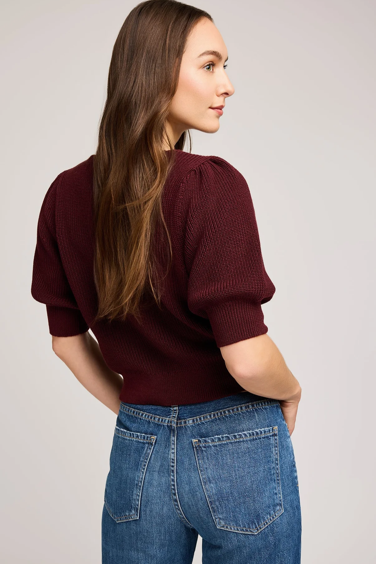 Woman wearing a burgundy sweater and blue jeans against a plain background