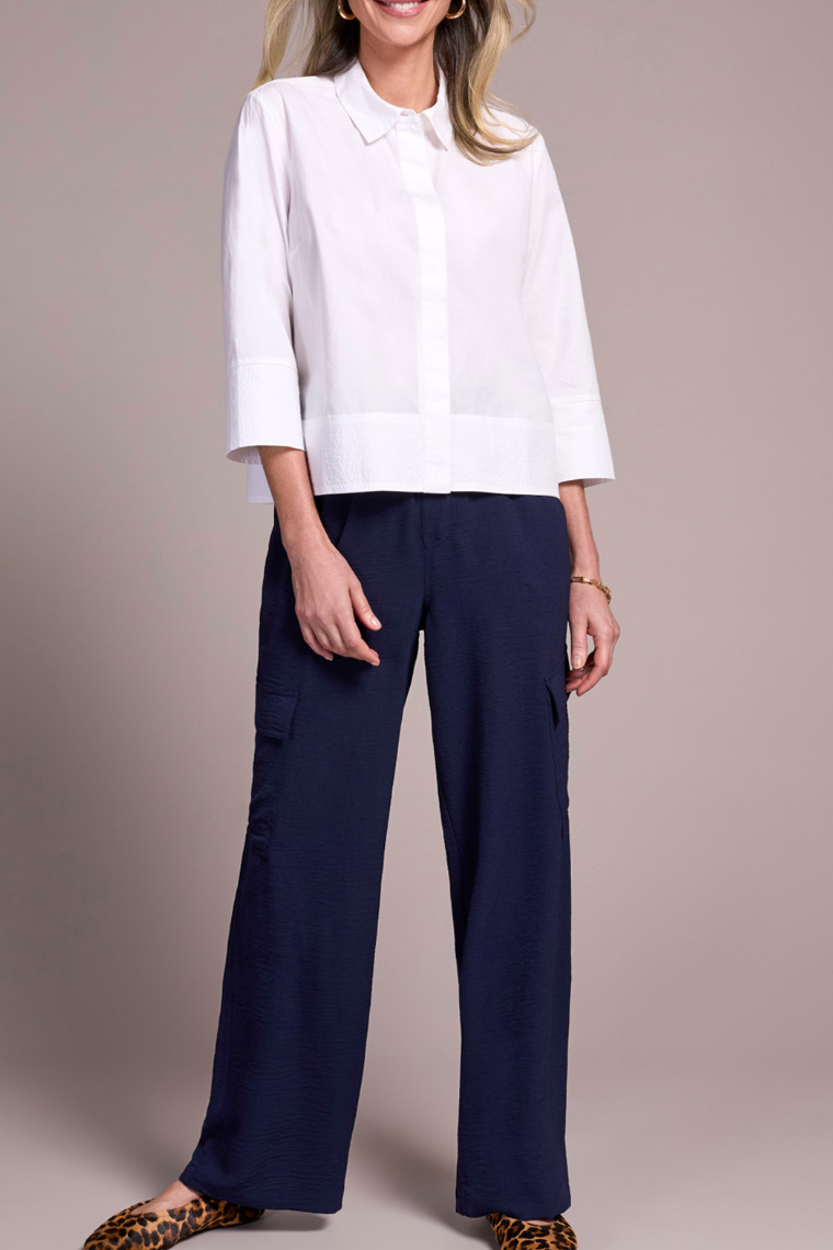 Person wearing a white blouse and navy pants on a beige background