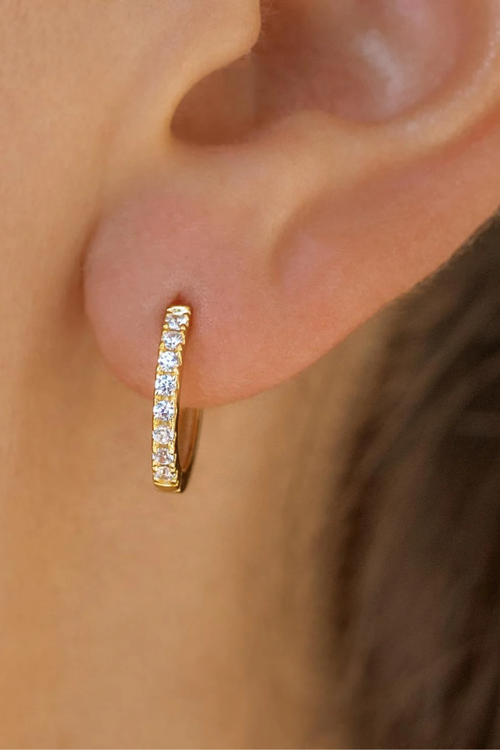 Gold hoop earring with clear stones worn by a person