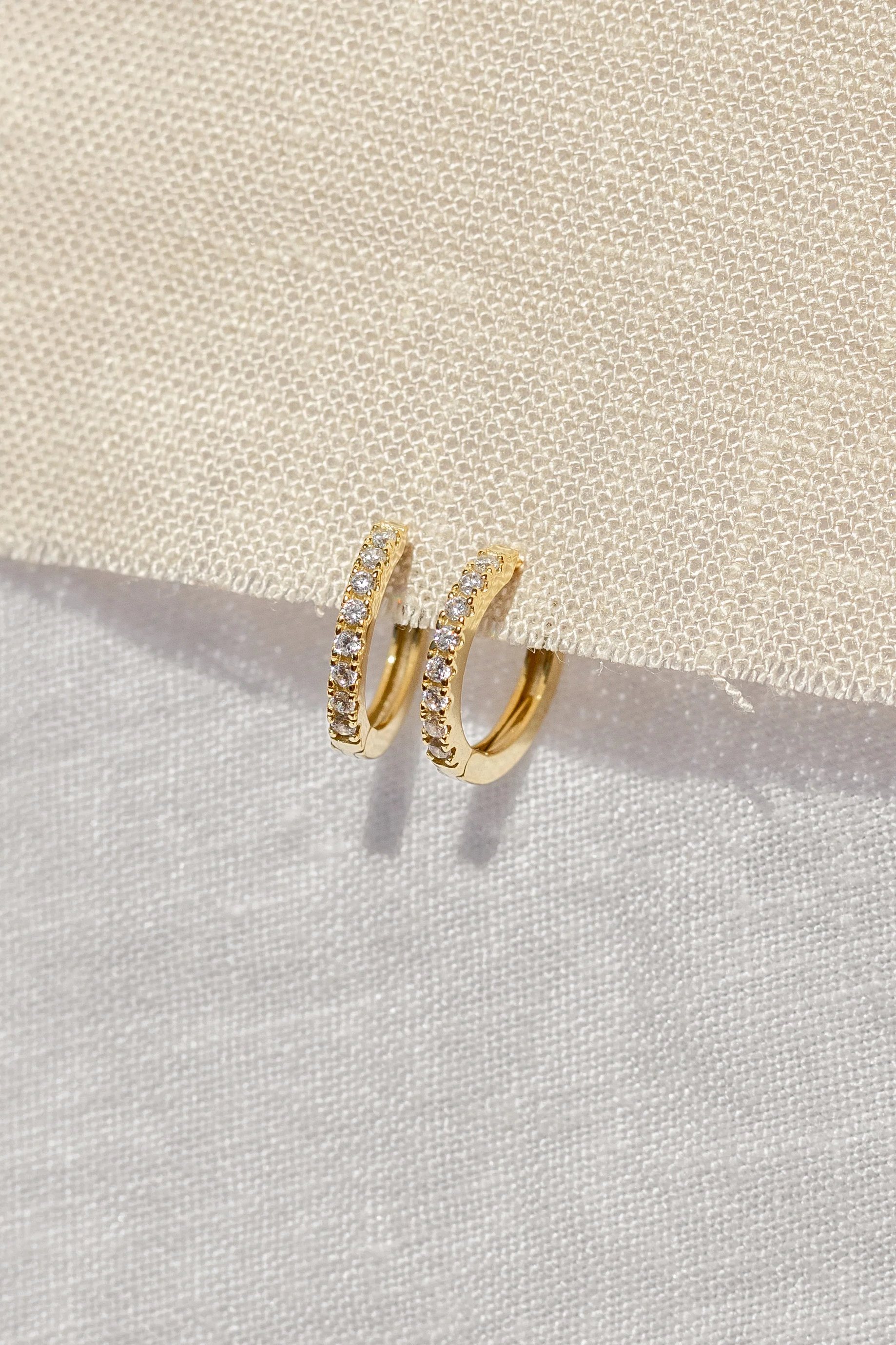 Gold hoop earrings with embedded stones on a textured beige surface