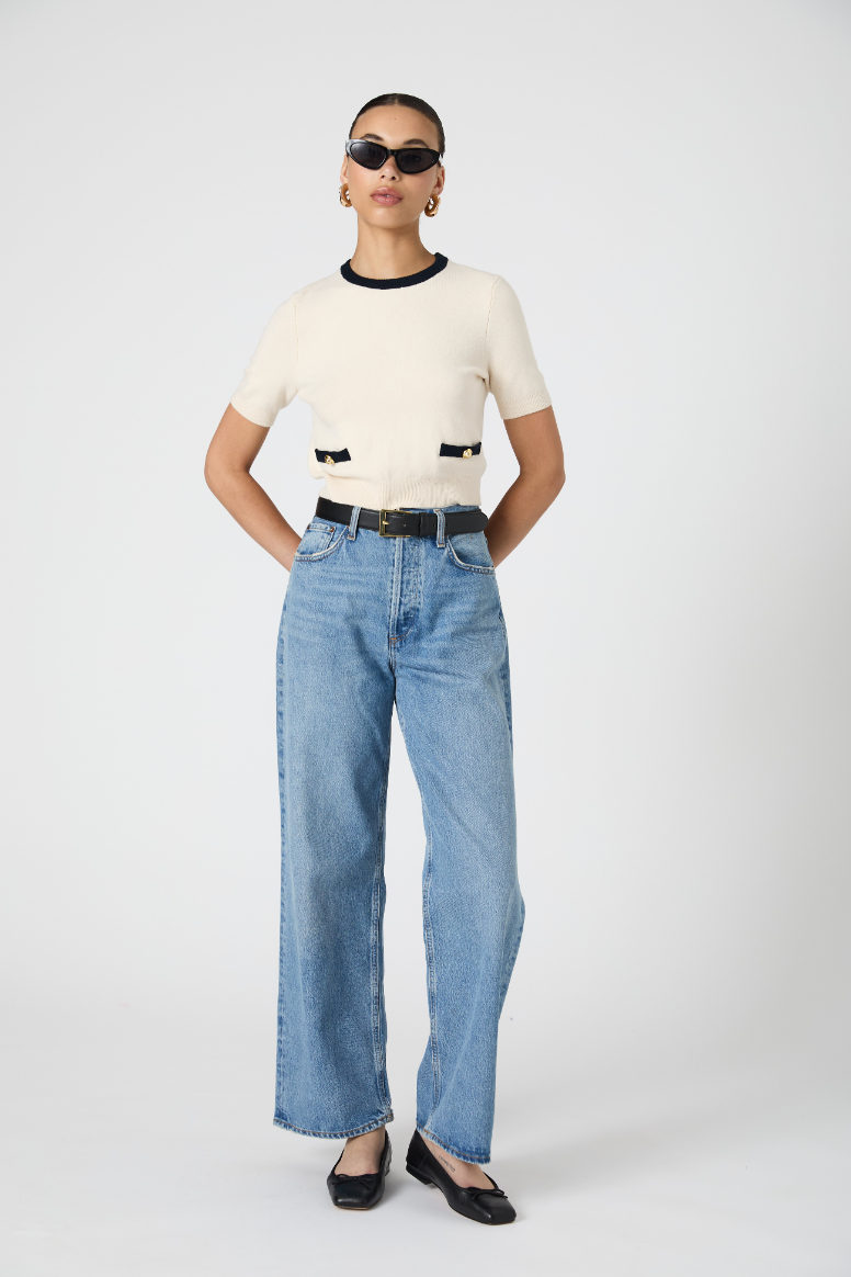 Person wearing a cream top and blue jeans on a white background