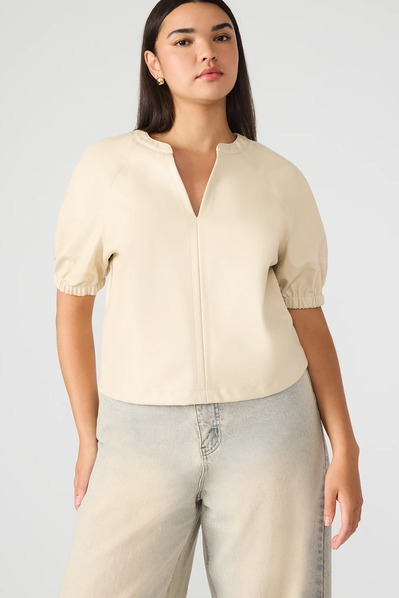 Woman wearing a beige short-sleeve blouse and light blue jeans on a white background