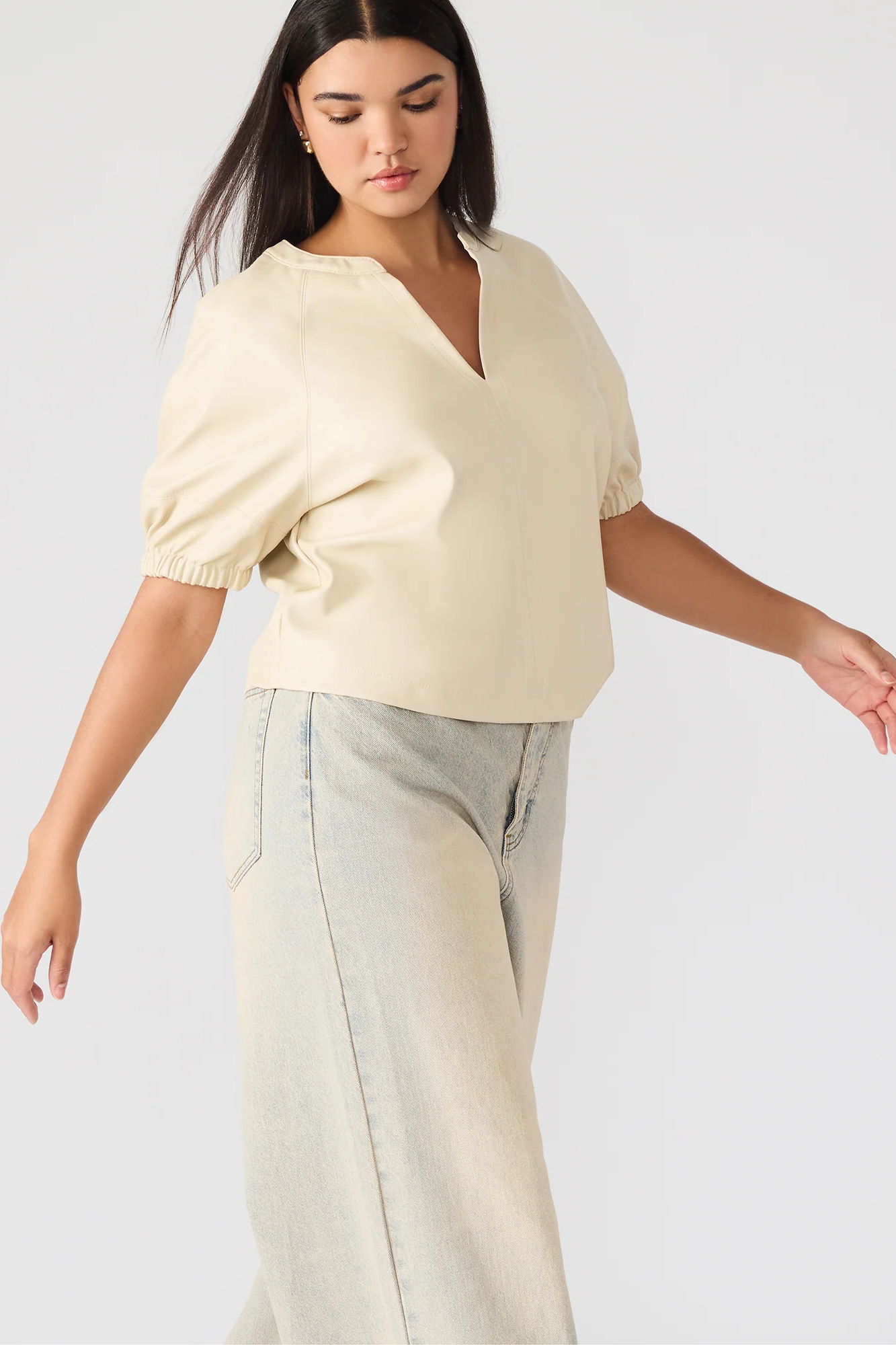 Woman wearing a light-colored blouse and light pants against a plain background
