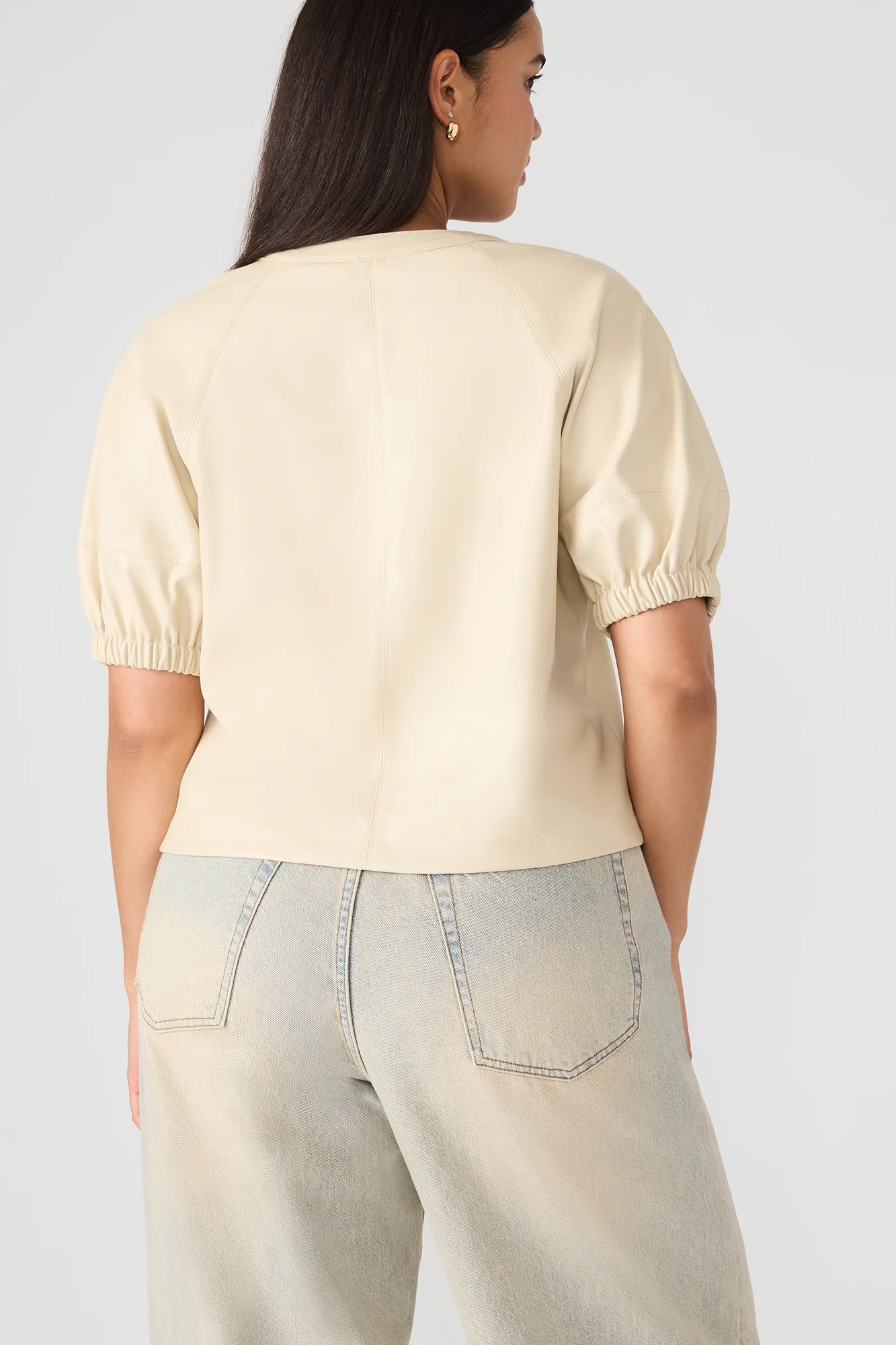 Woman wearing a beige top and light blue jeans against a plain background