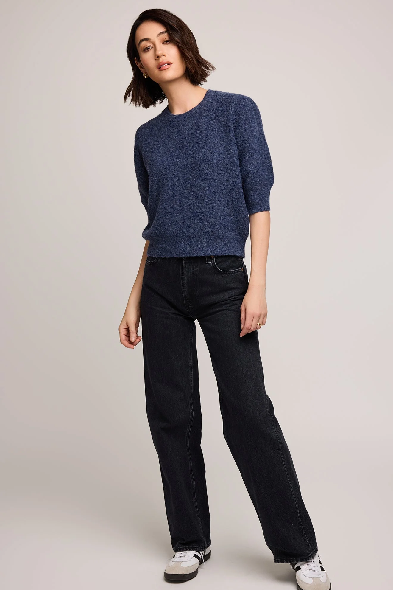 Woman wearing a blue sweater and black jeans on a plain background