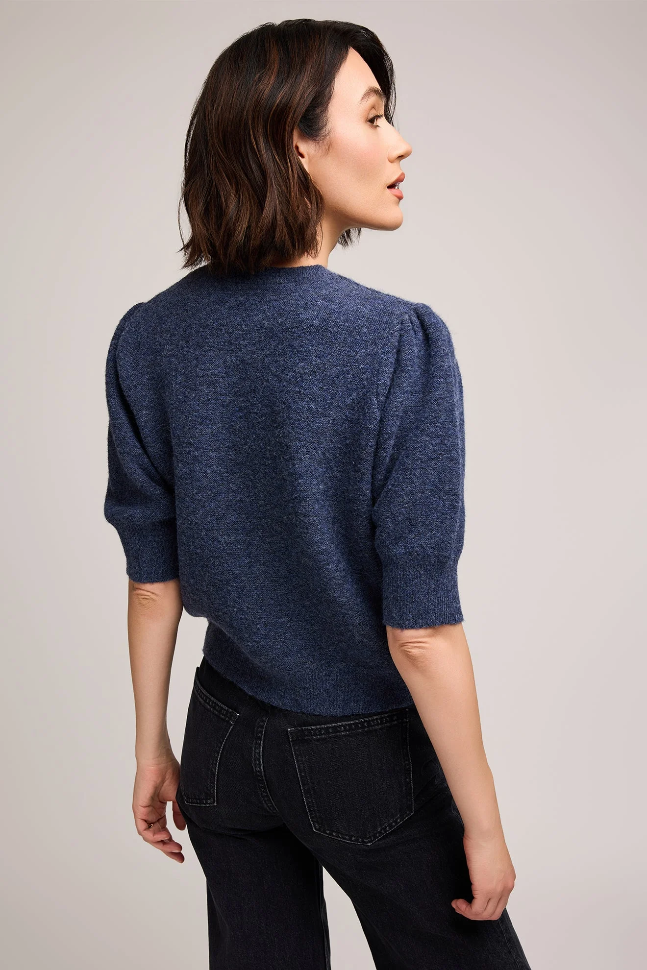 Woman wearing a blue sweater and black pants against a plain background