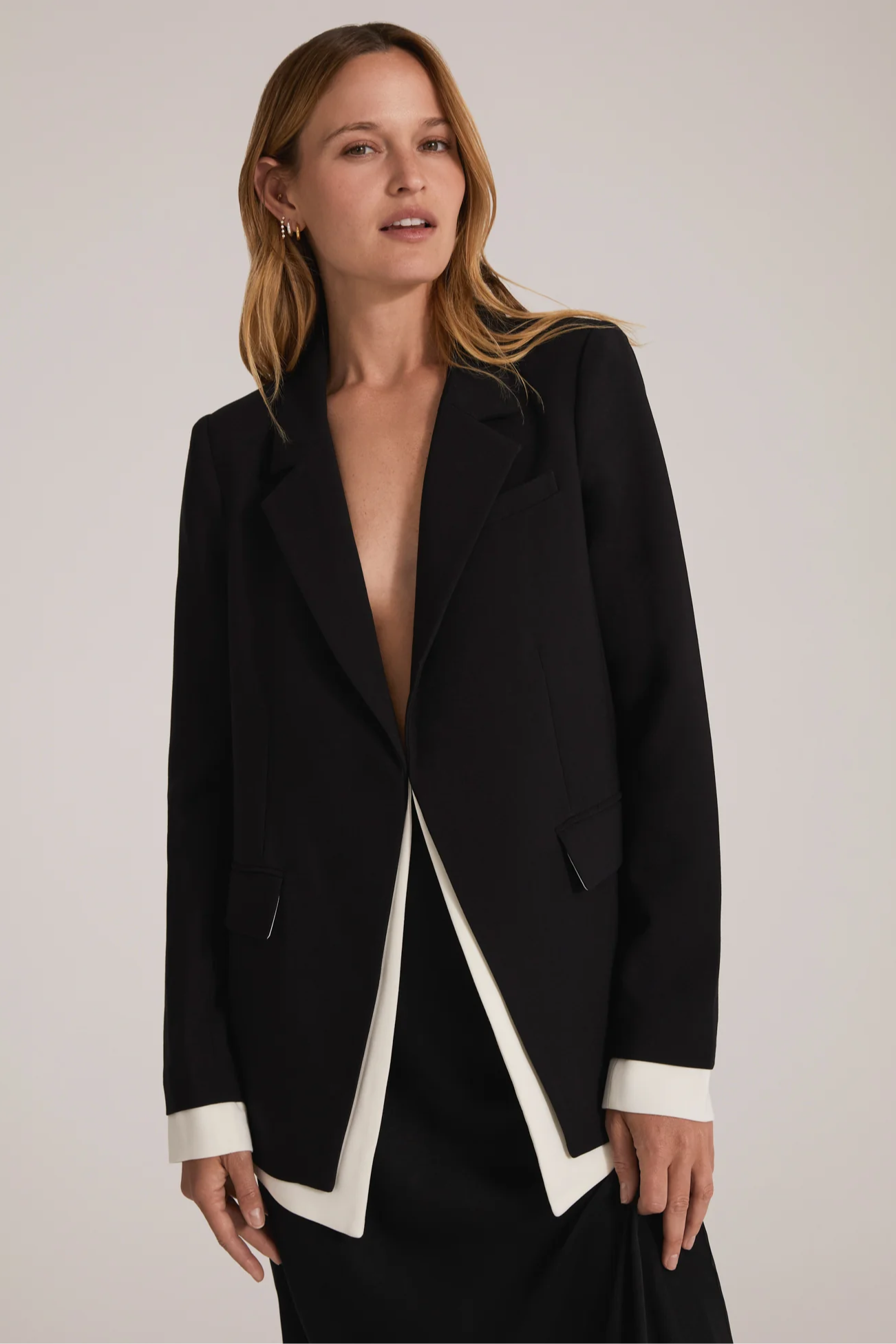 Woman wearing a black blazer with white trim on a plain background