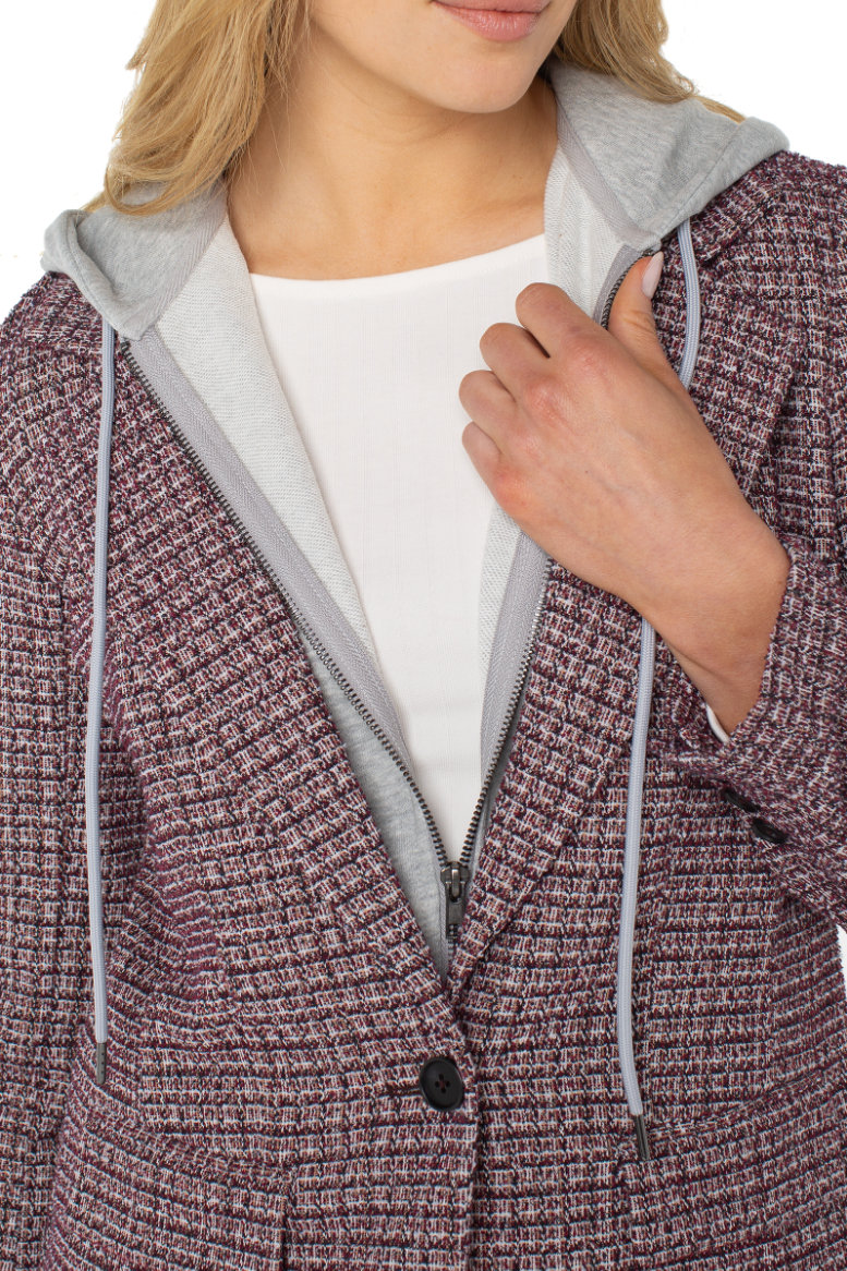 Close-up of a person wearing a textured purple coat with a gray hood and white shirt underneath.