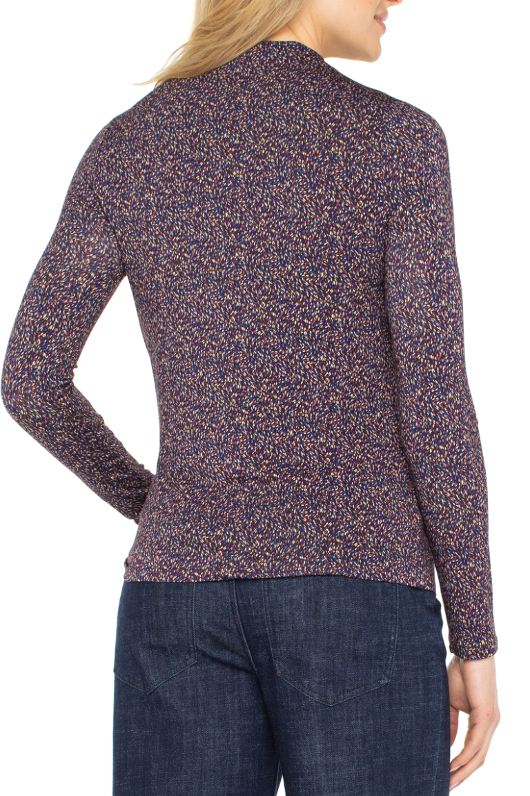 Woman wearing a patterned long-sleeve top and dark jeans on a white background