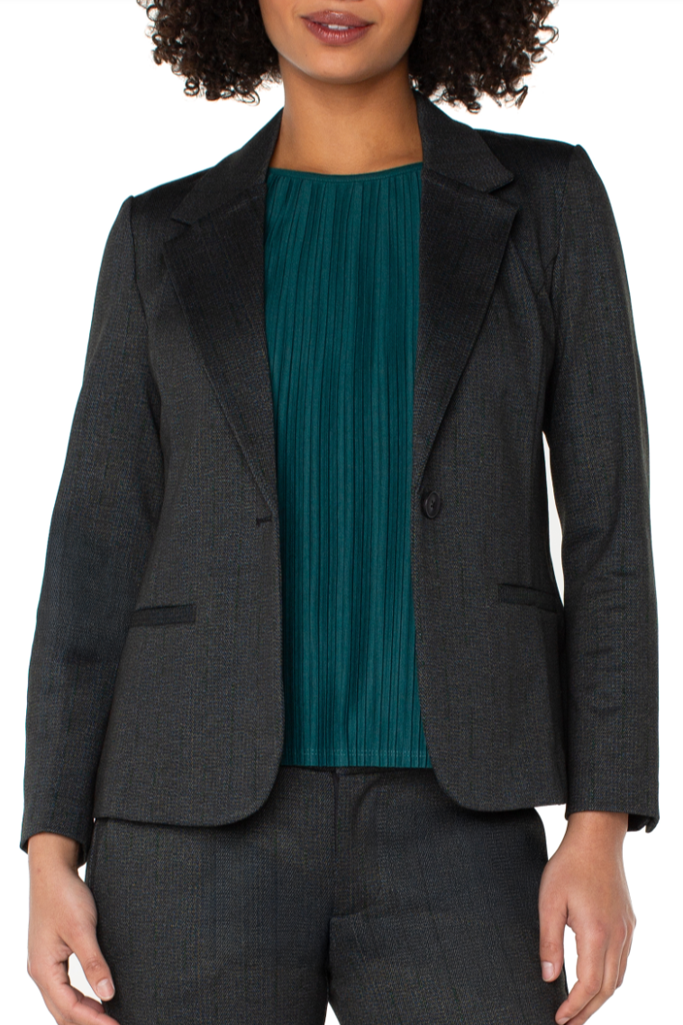 Person wearing a dark gray blazer over a teal top on a white background
