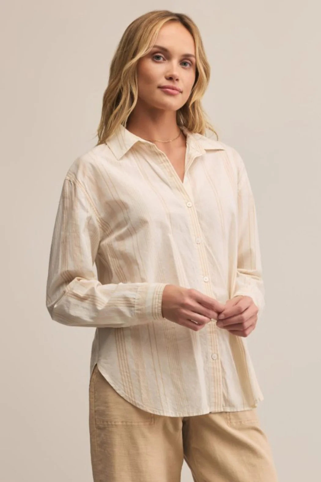 Woman wearing a light-colored shirt and pants against a plain background