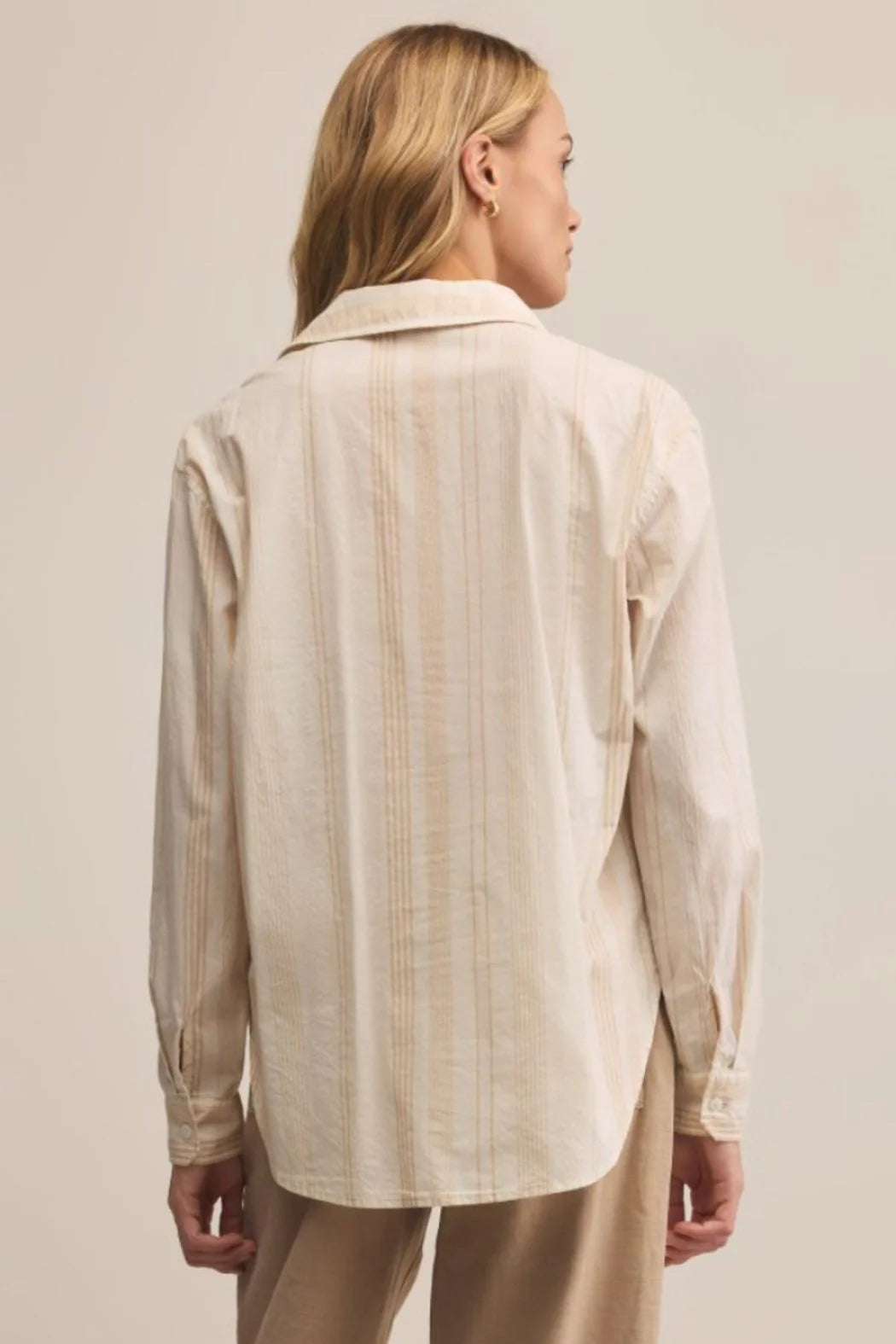 Woman wearing a beige striped shirt and pants against a plain background