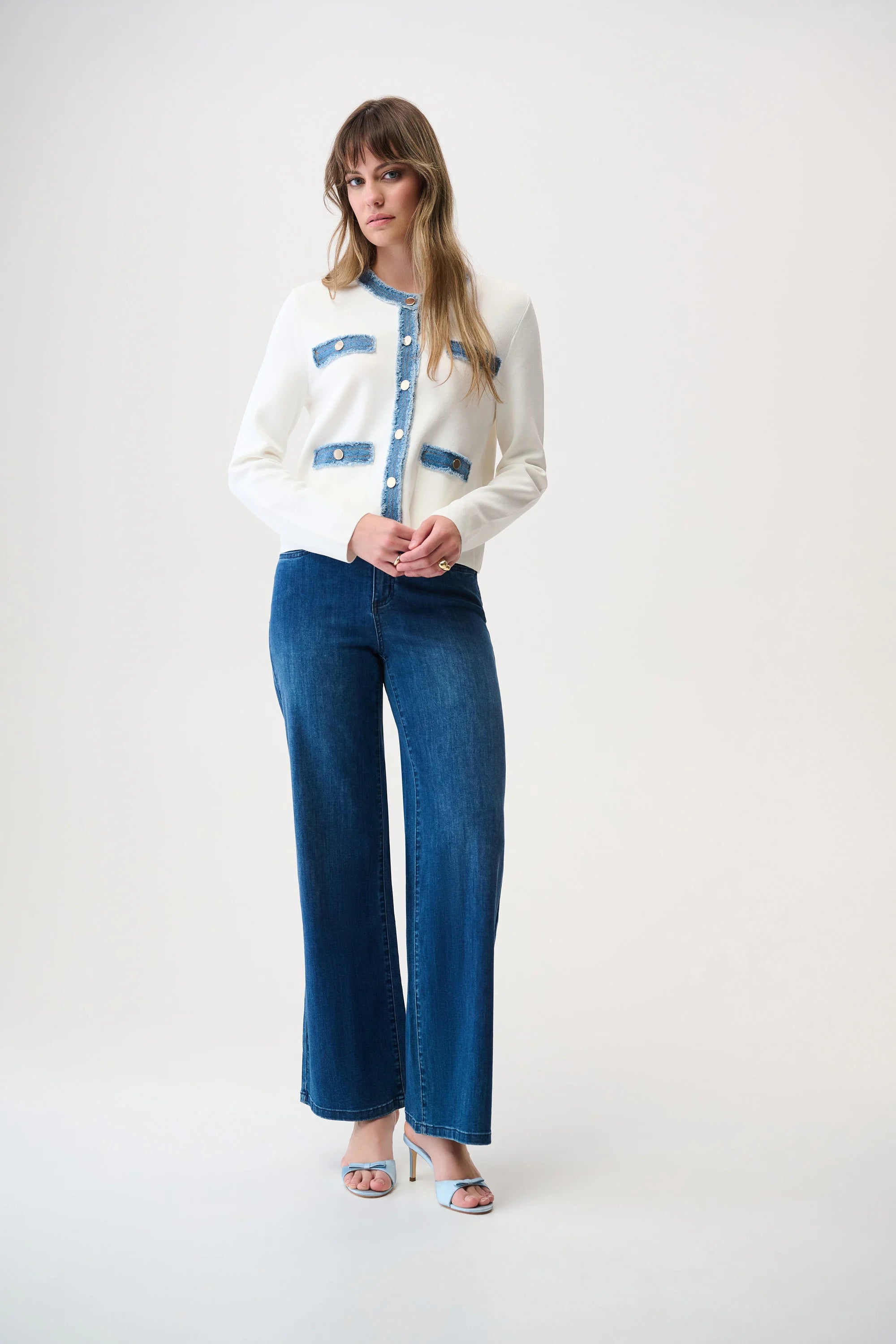 Woman wearing a white sweater with blue accents and blue jeans on a white background