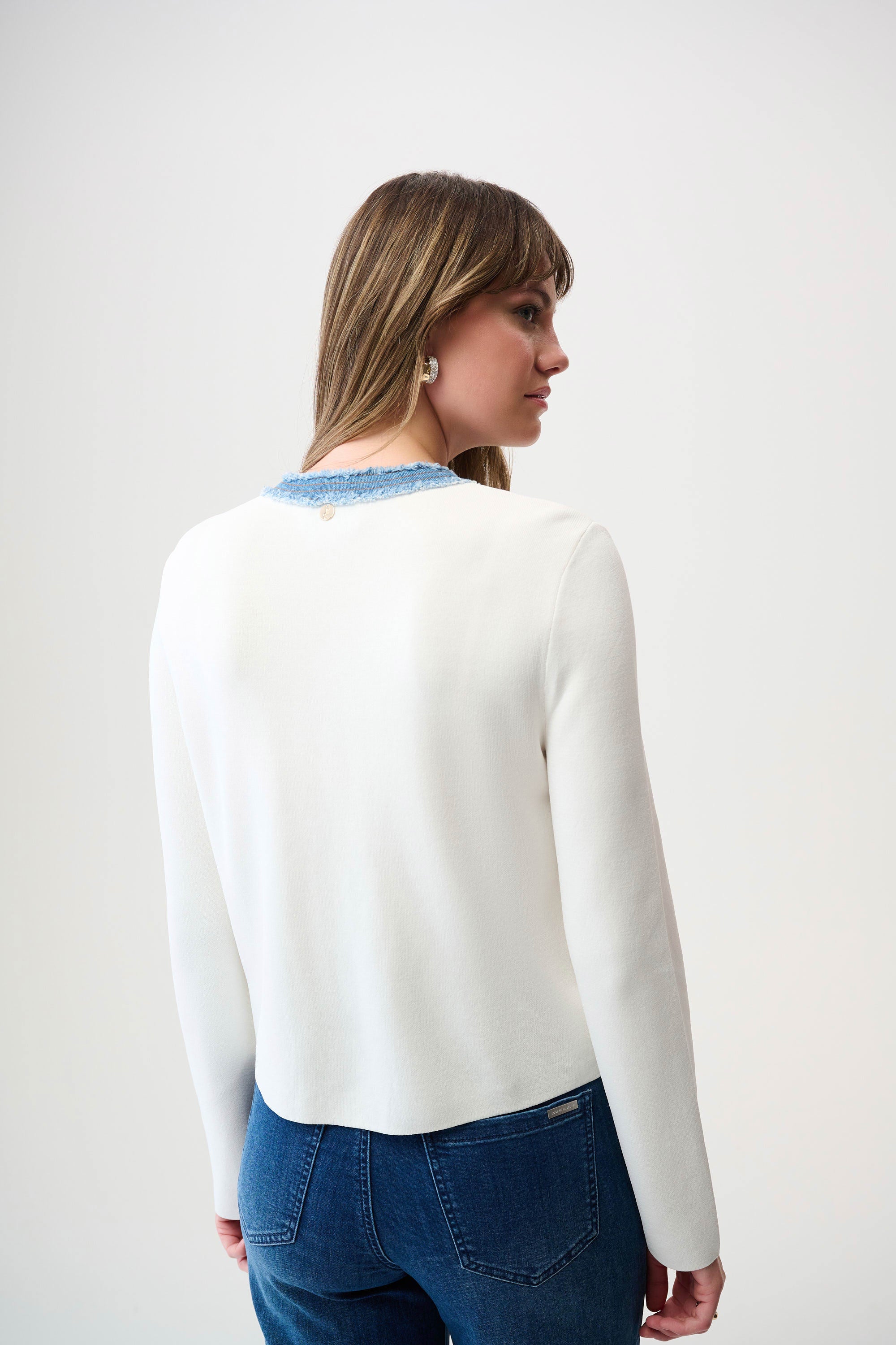 Woman wearing a white long-sleeve top with blue trim on a plain background