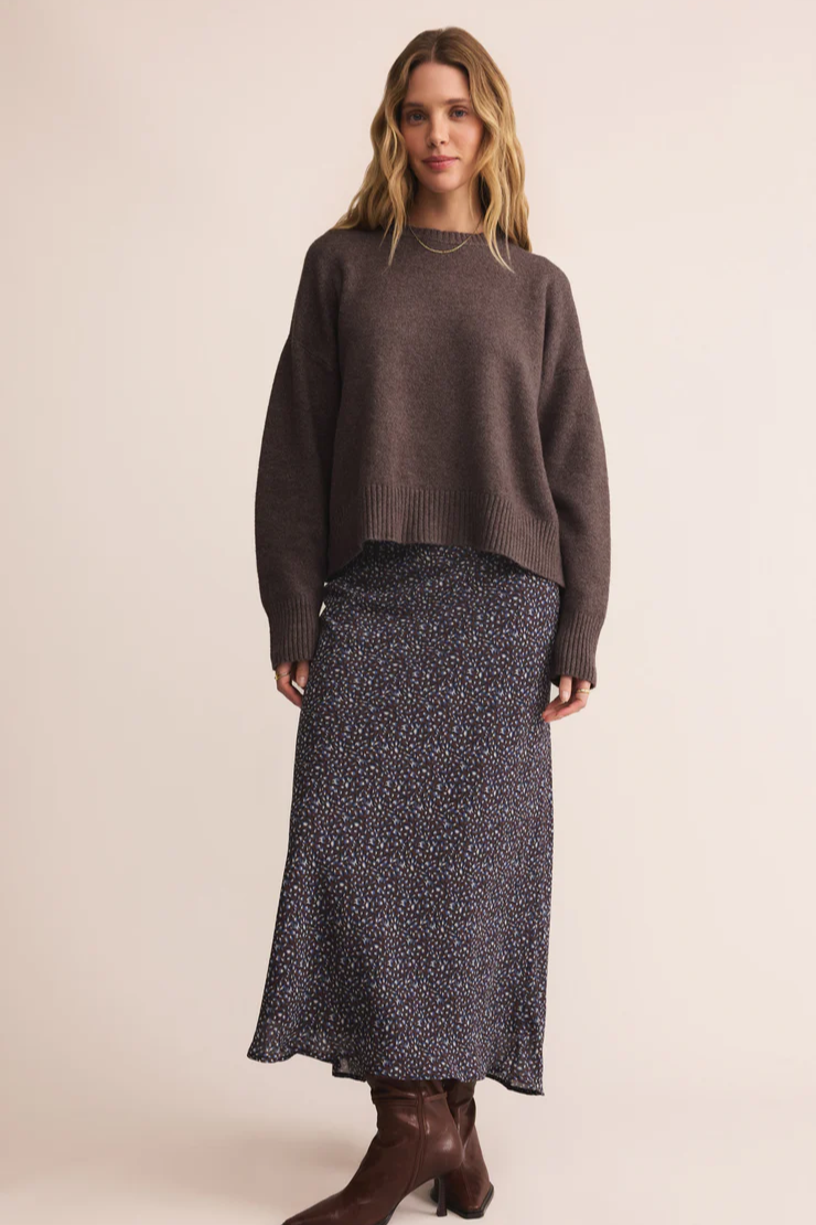 Woman wearing a brown sweater and patterned skirt on a beige background