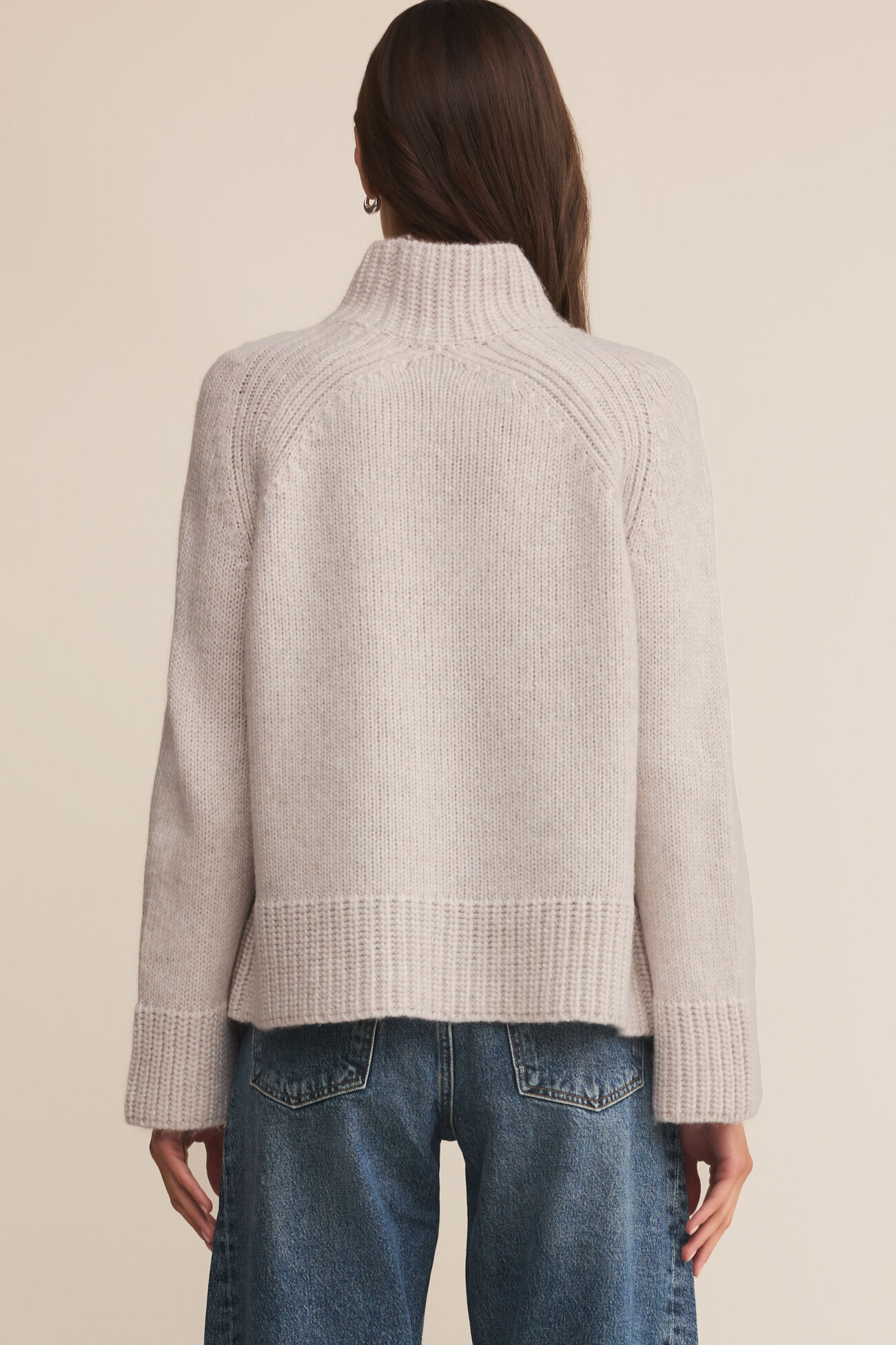 Person wearing a beige ribbed sweater and blue jeans on a beige background