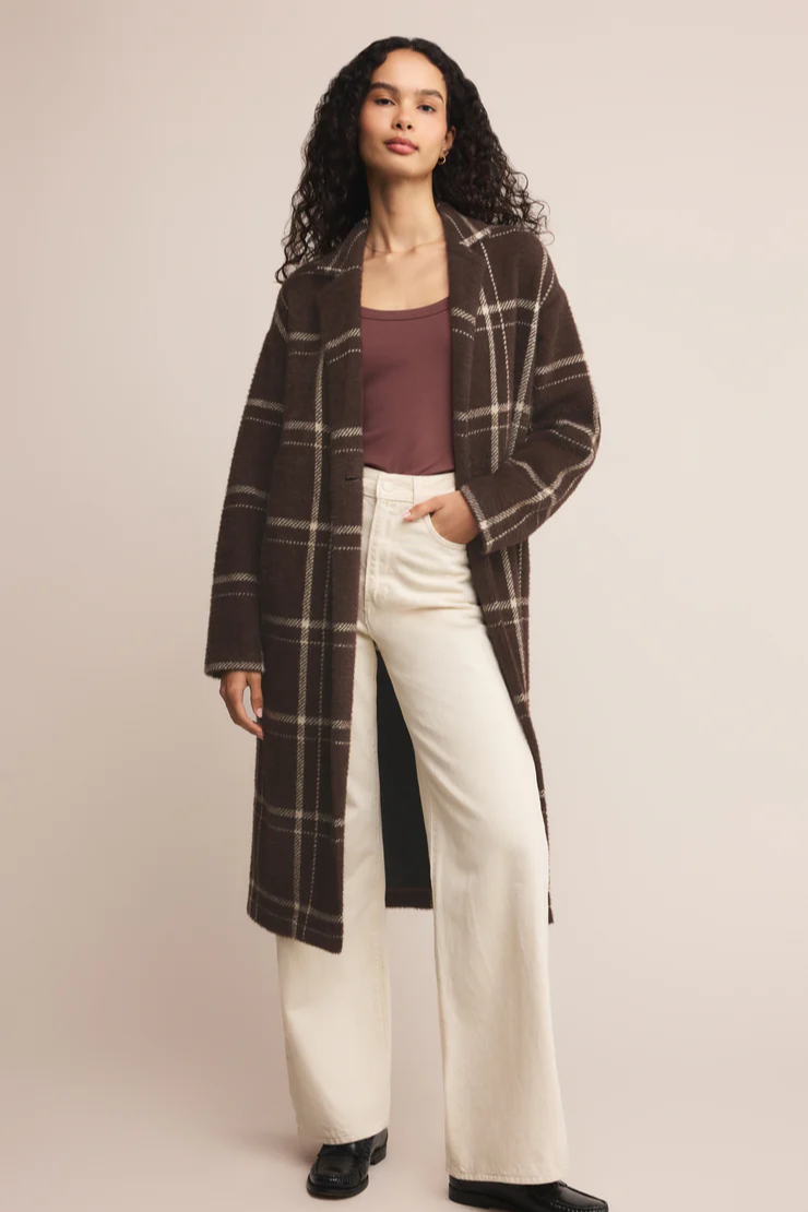 Woman wearing a plaid coat, burgundy top, and white pants on a beige background