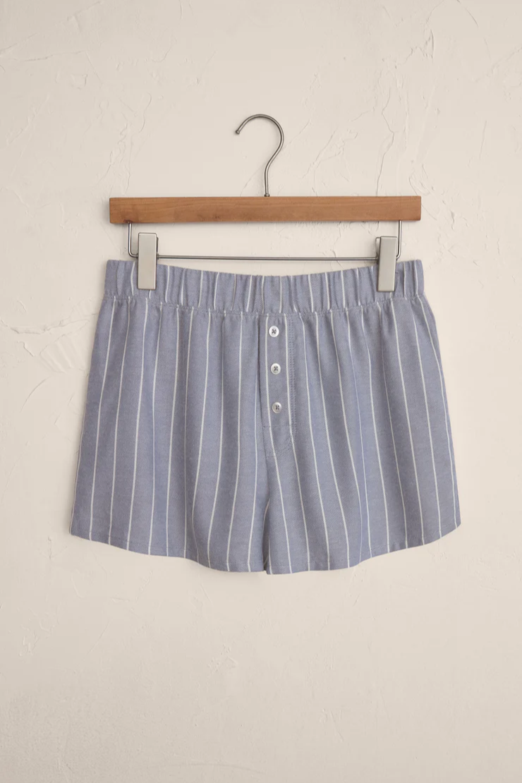 Blue and white striped shorts on a wooden hanger against a beige wall.