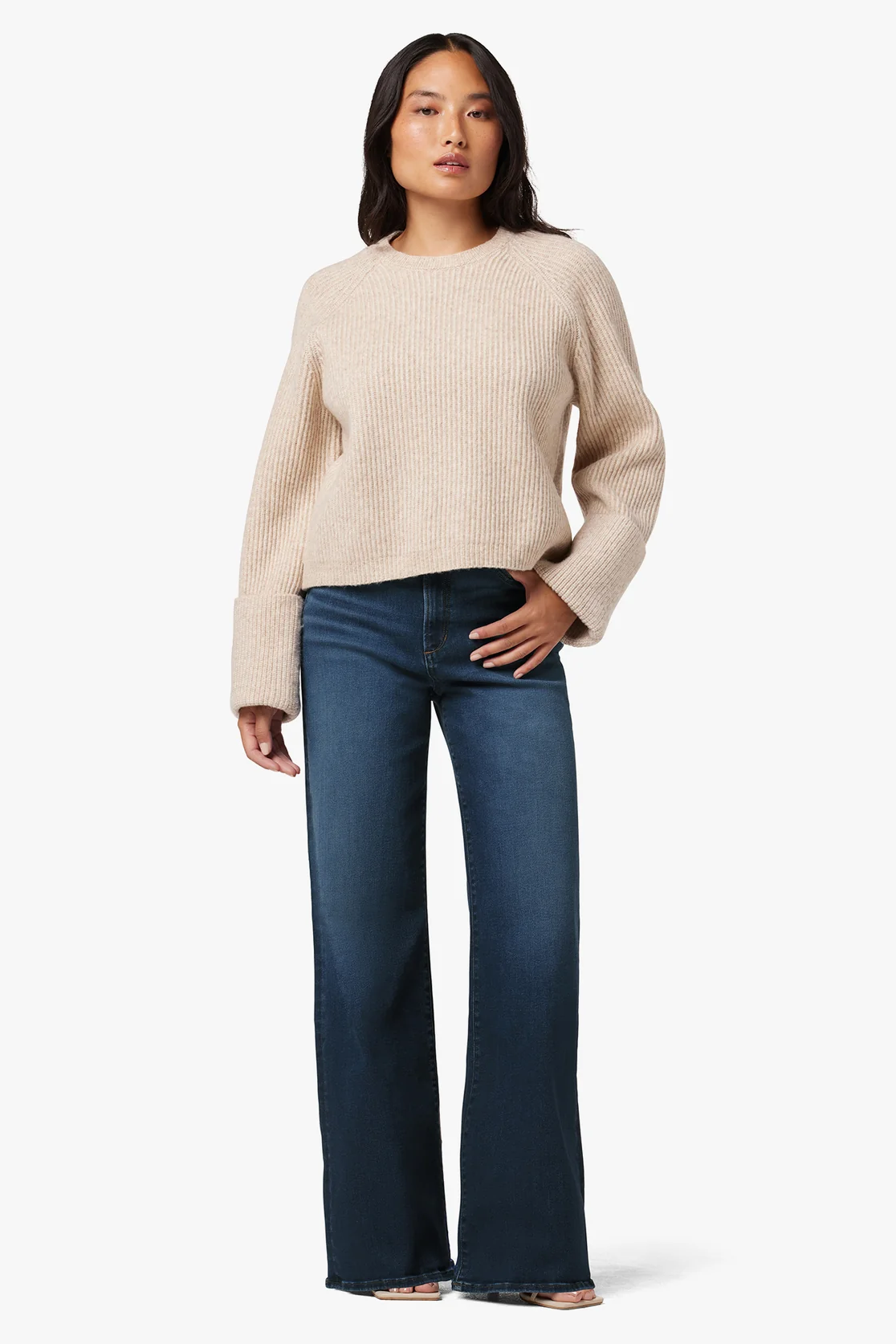 Woman wearing a beige sweater and blue jeans on a white background