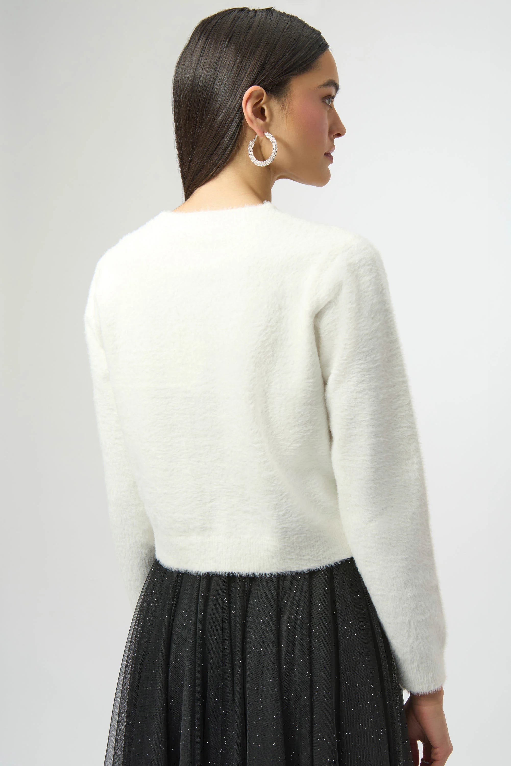 Woman wearing a white sweater and black skirt on a plain background