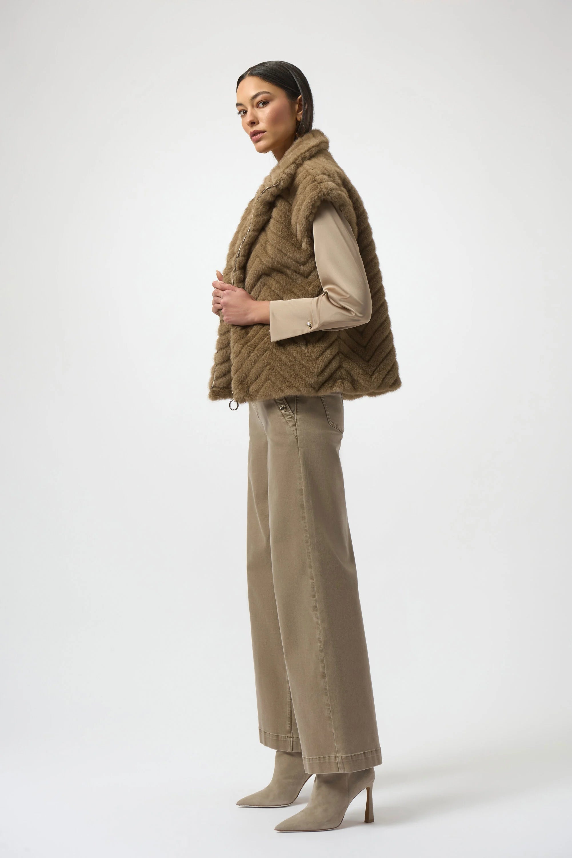 Woman wearing a brown faux fur vest and beige pants on a white background
