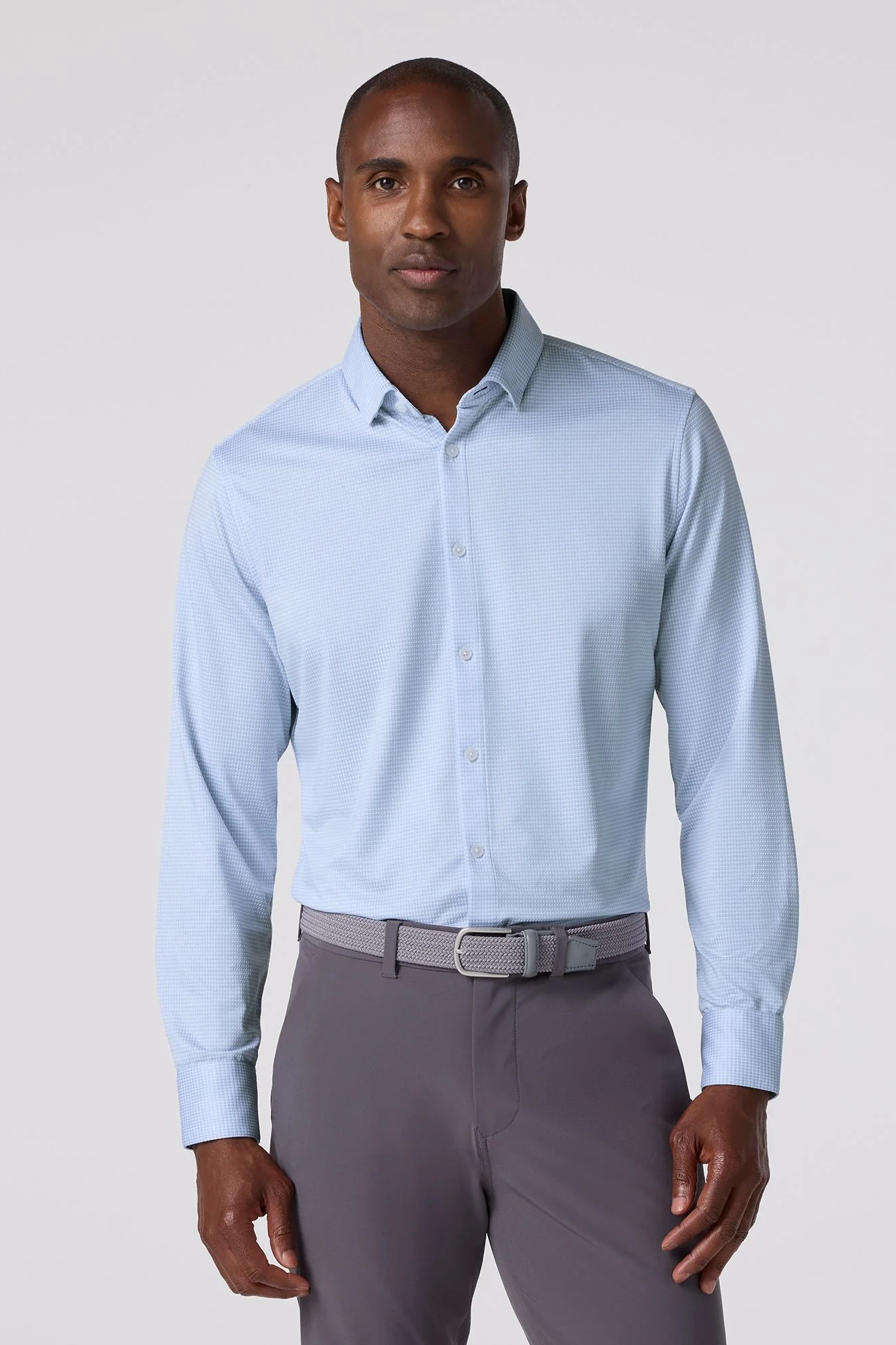 Man wearing a light blue dress shirt and gray pants on a plain background
