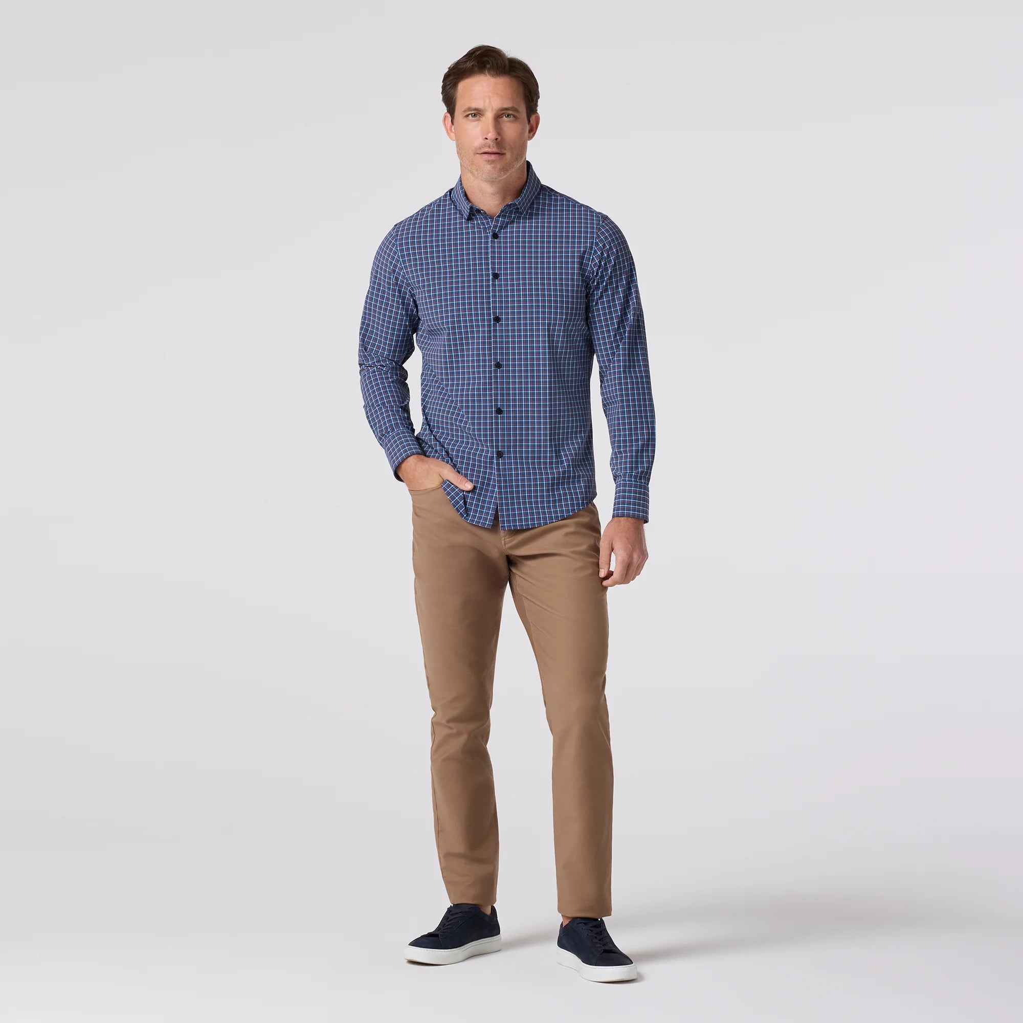 Man wearing a blue checkered shirt and brown pants on a white background