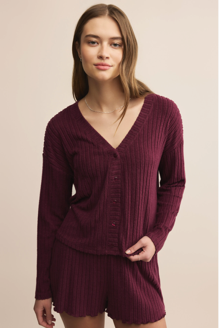 Woman wearing a ribbed burgundy sweater and shorts set against a beige background