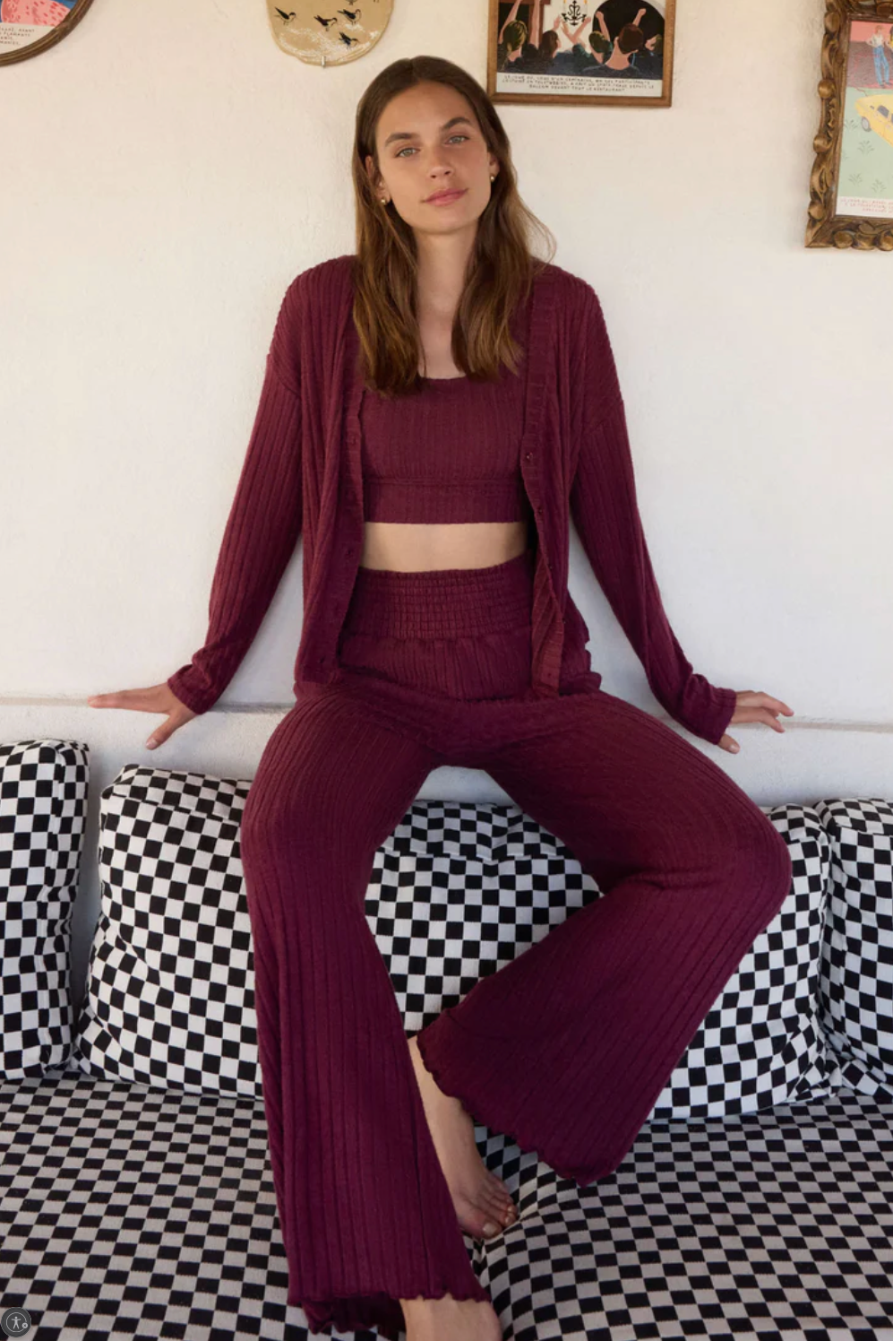 Woman in a burgundy outfit sitting on a checkered couch with a white wall and framed pictures in the background.