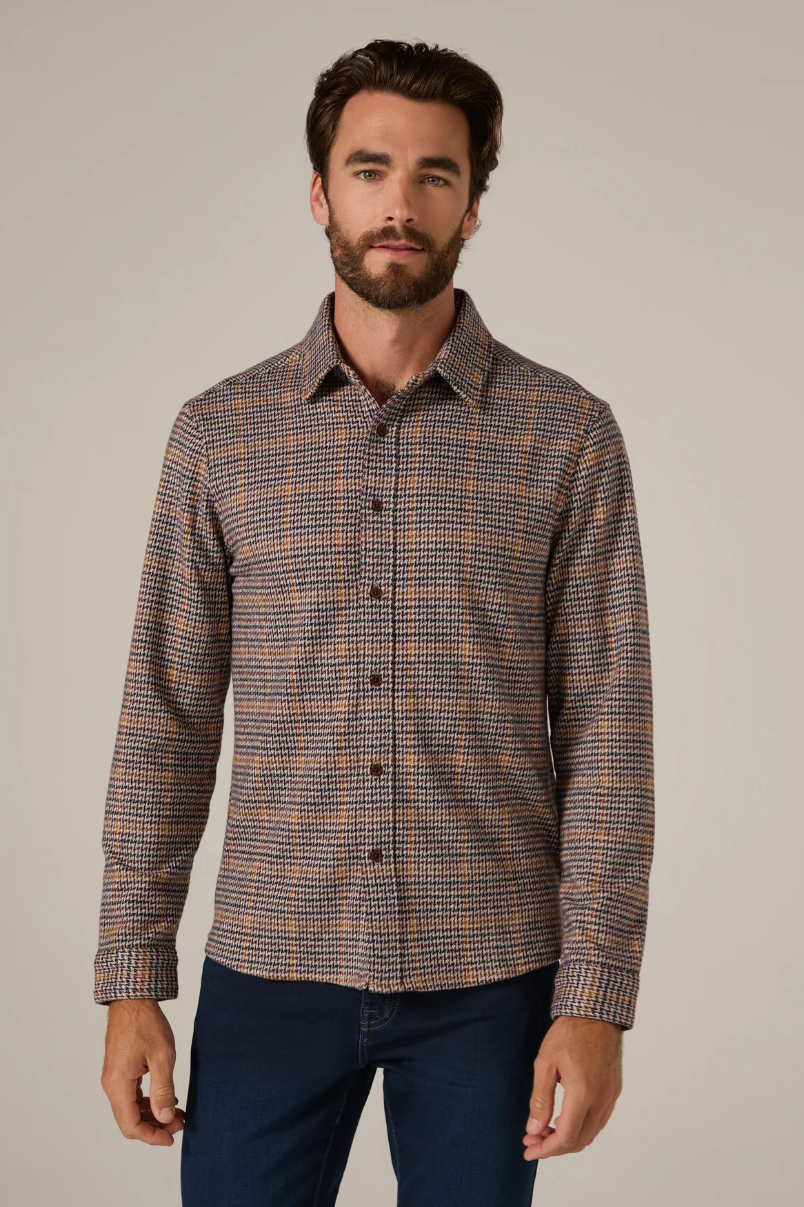 Man wearing a patterned shirt and dark pants against a neutral background