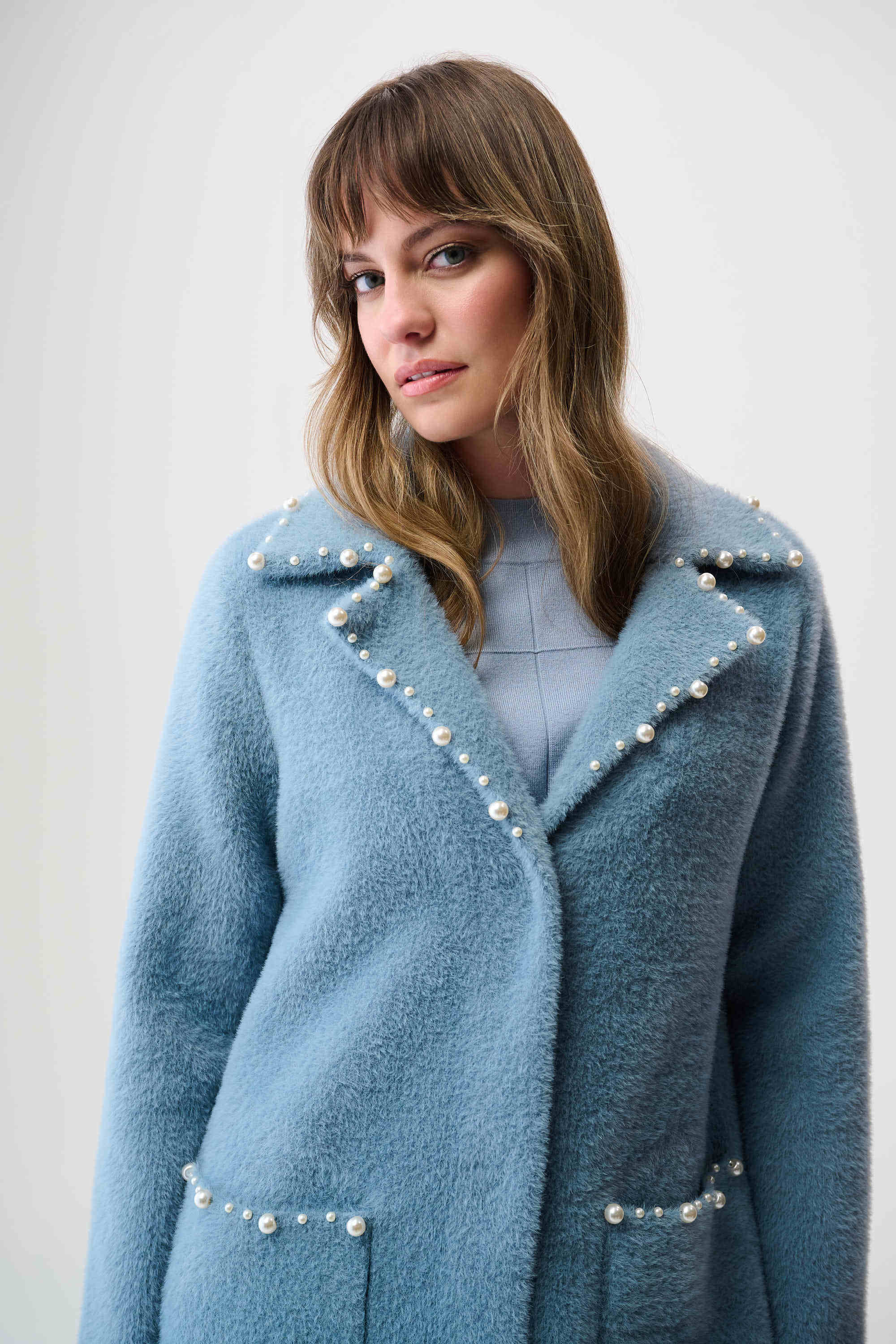 Woman wearing a blue coat with pearl embellishments against a white background