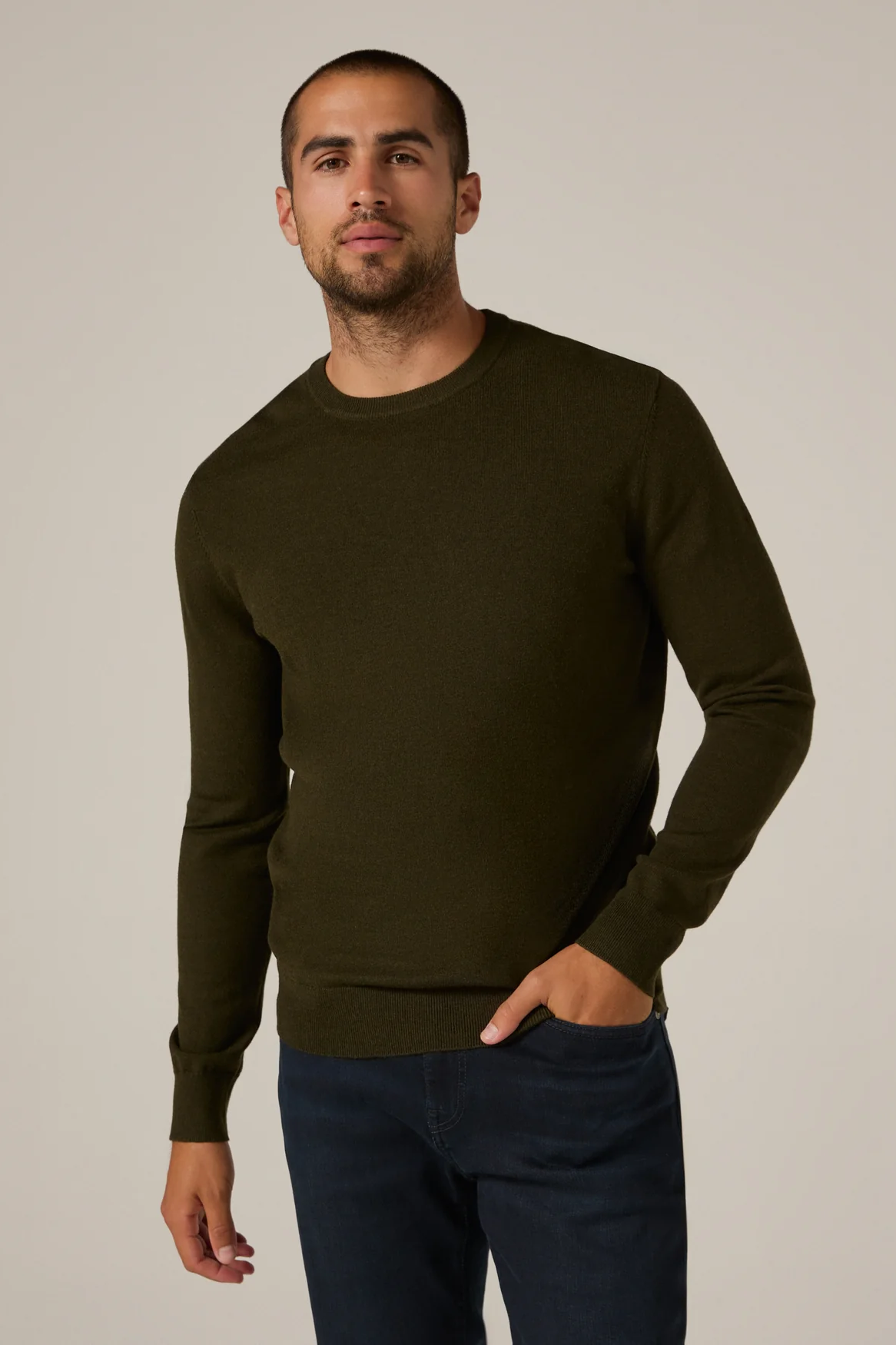 Man wearing a dark green sweater and blue jeans against a plain background