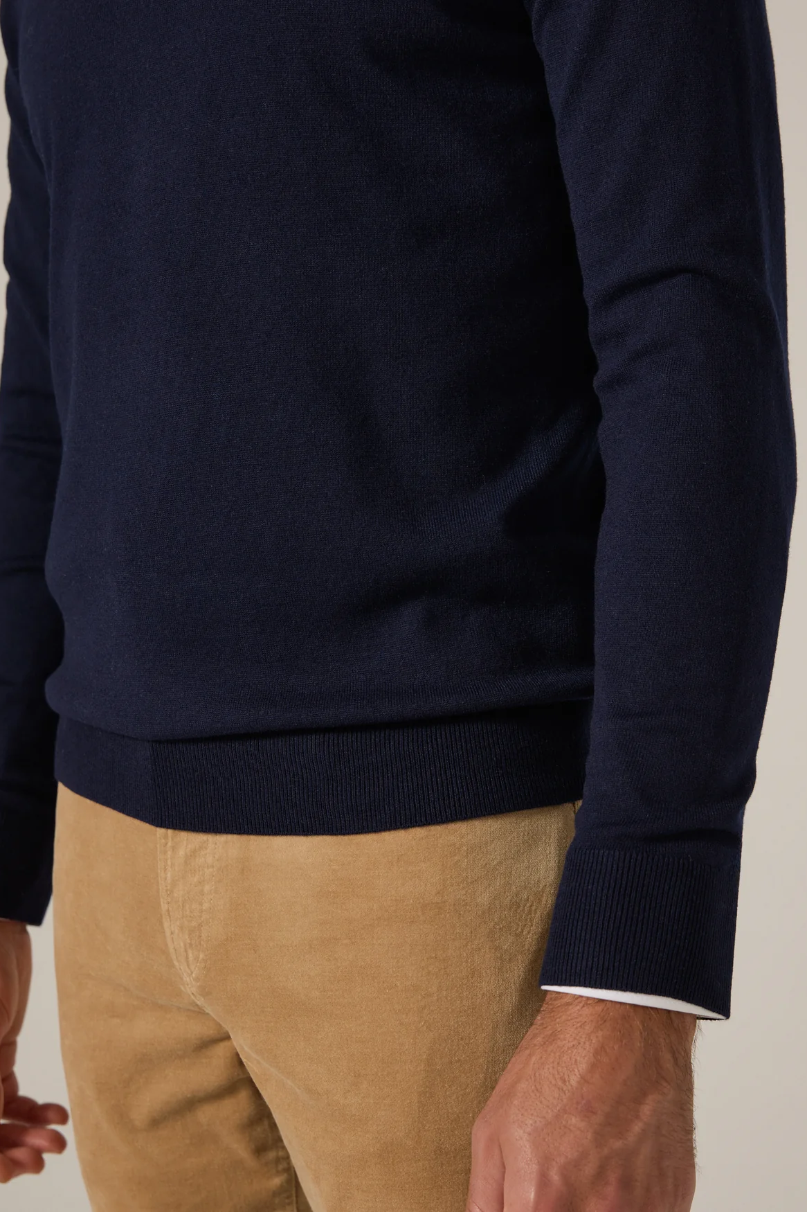 Navy sweater worn by a person with beige pants on a neutral background