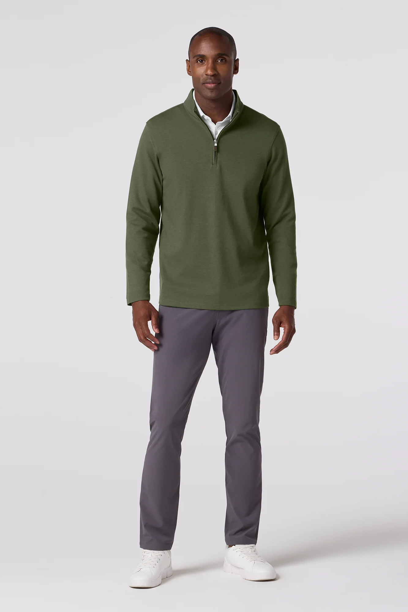 Man wearing a green quarter-zip sweater and gray pants on a white background