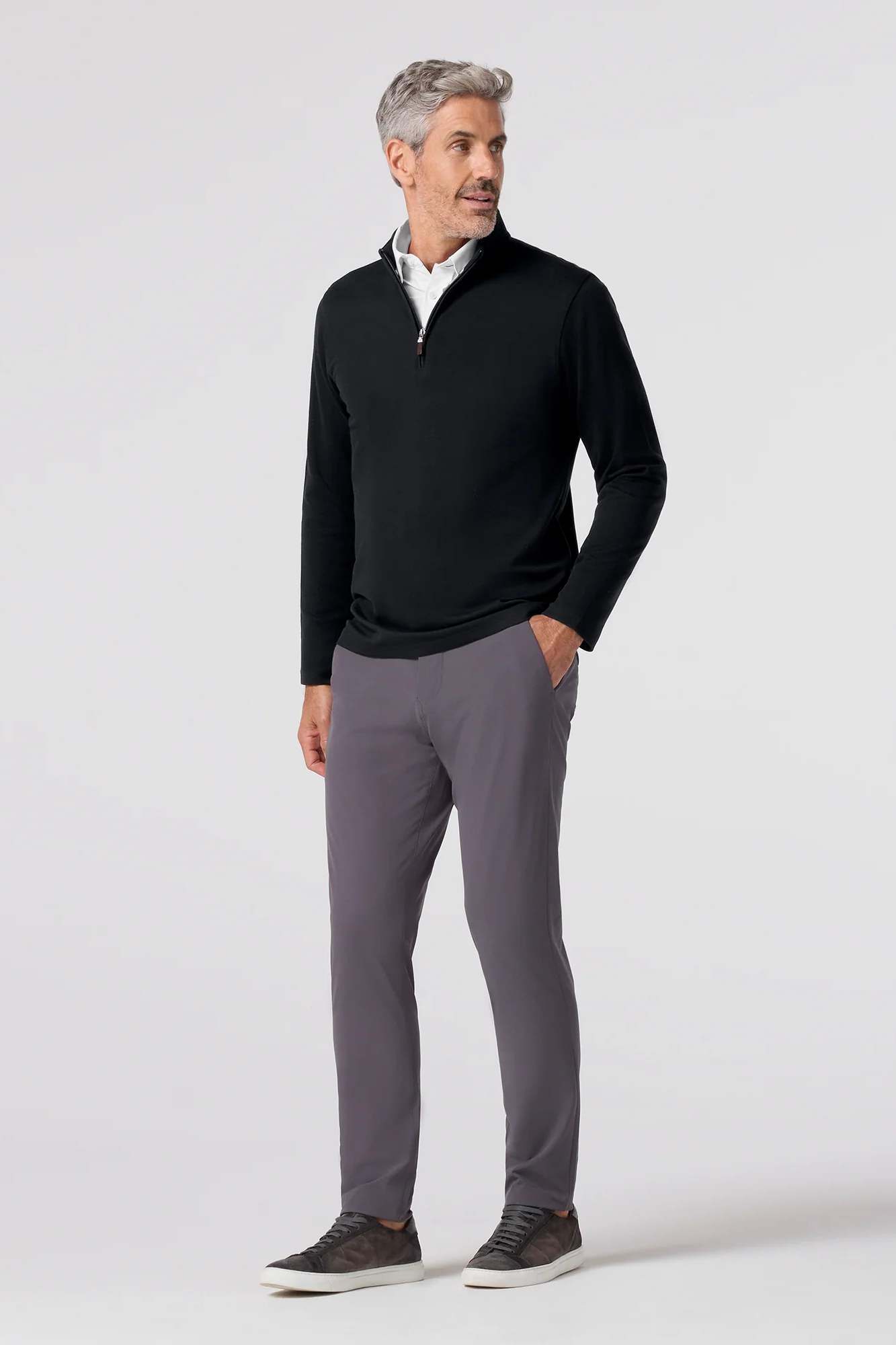 Man wearing a black quarter-zip sweater and gray pants on a white background