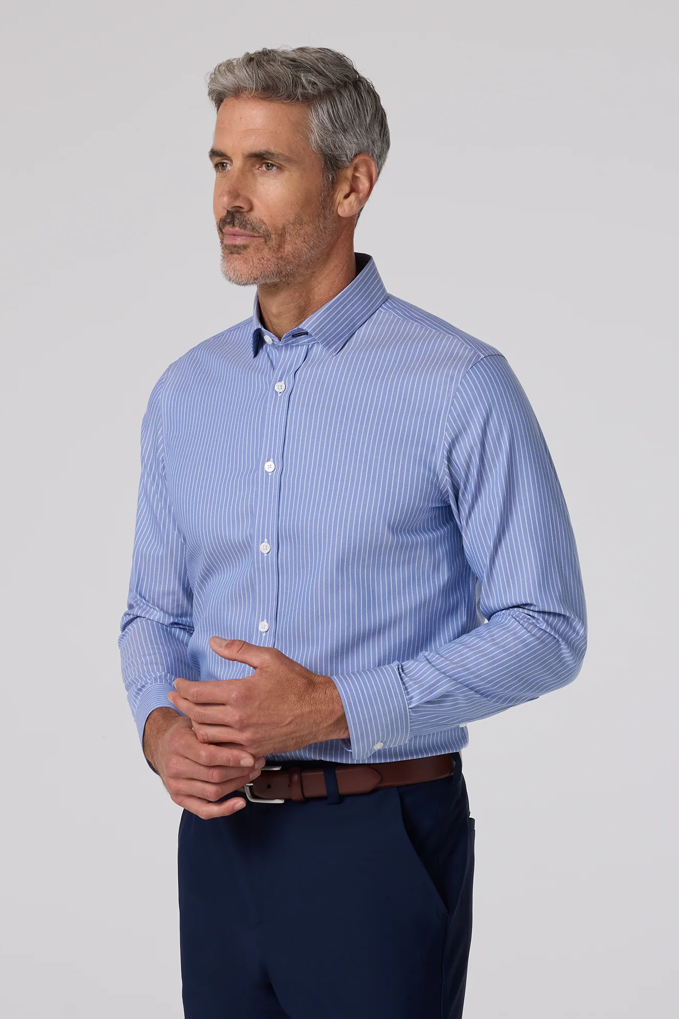 Man wearing a blue striped shirt and dark pants on a light gray background