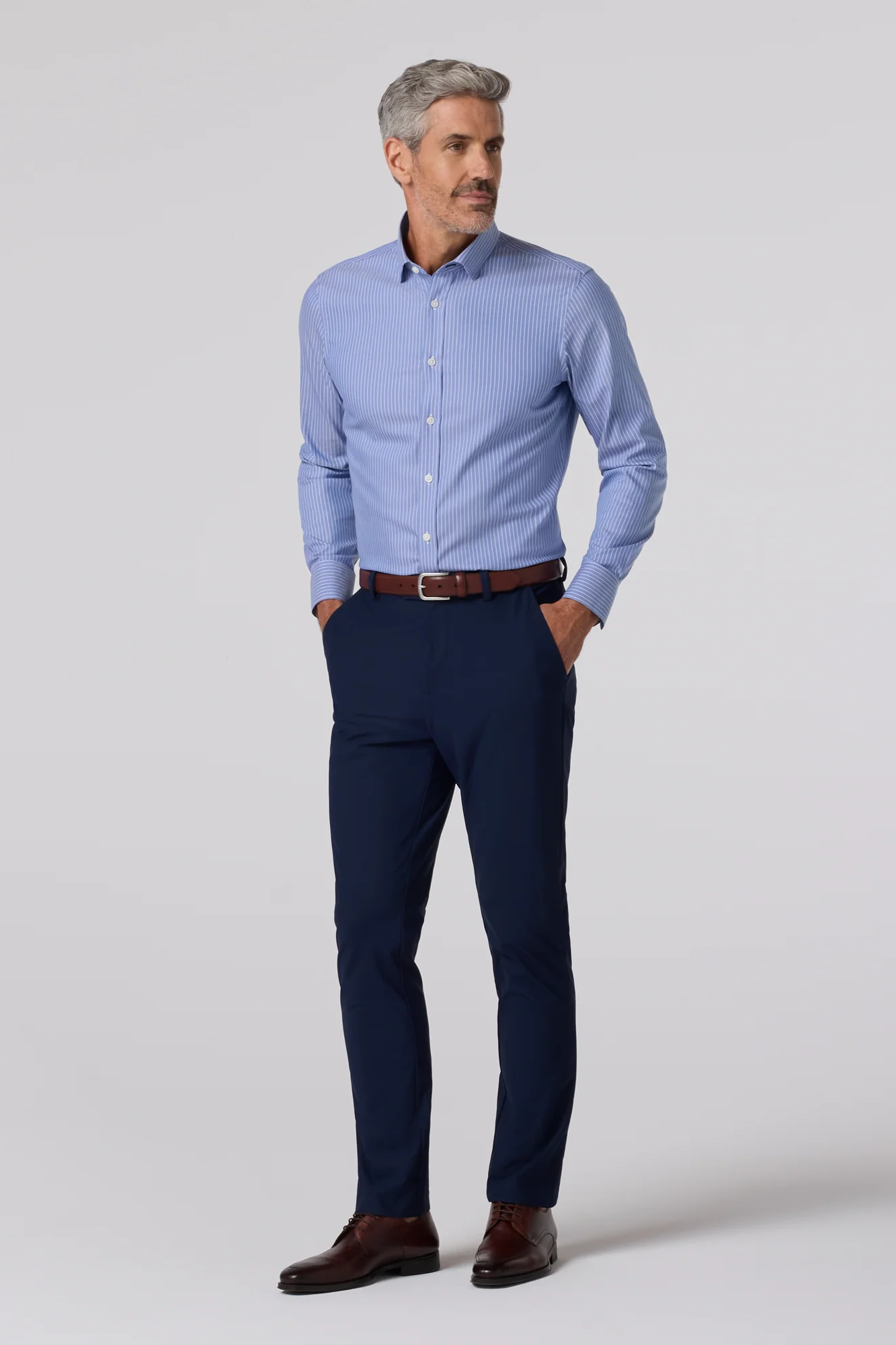 Man wearing a light blue dress shirt and navy pants on a white background