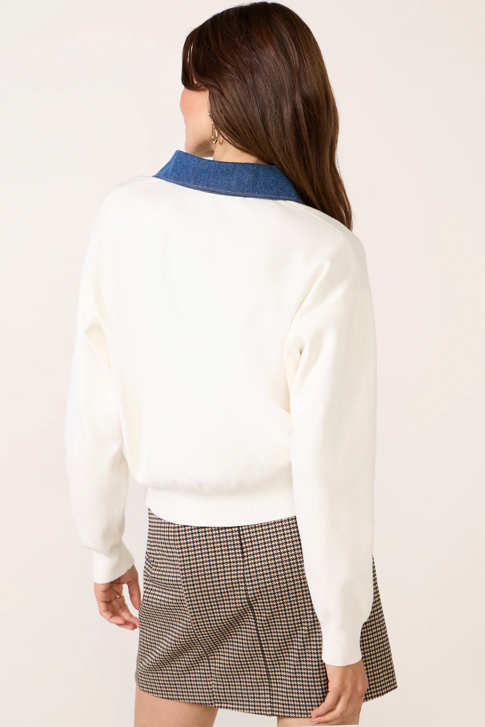 Woman wearing a white sweater with blue collar and plaid skirt on a plain background