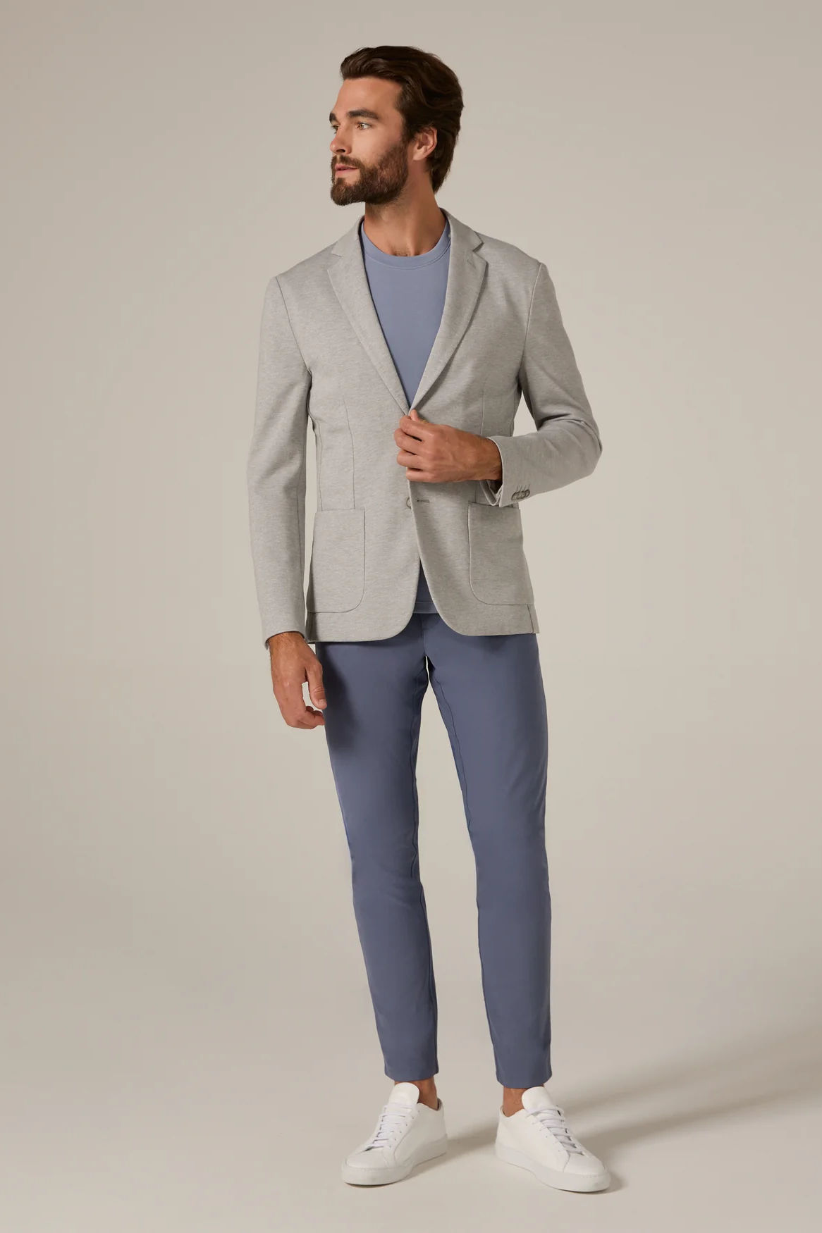 Man wearing a light gray blazer and blue pants on a plain background