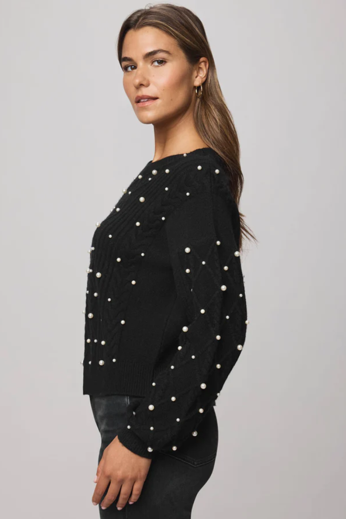 Woman wearing a black sweater with white pearl embellishments on a gray background