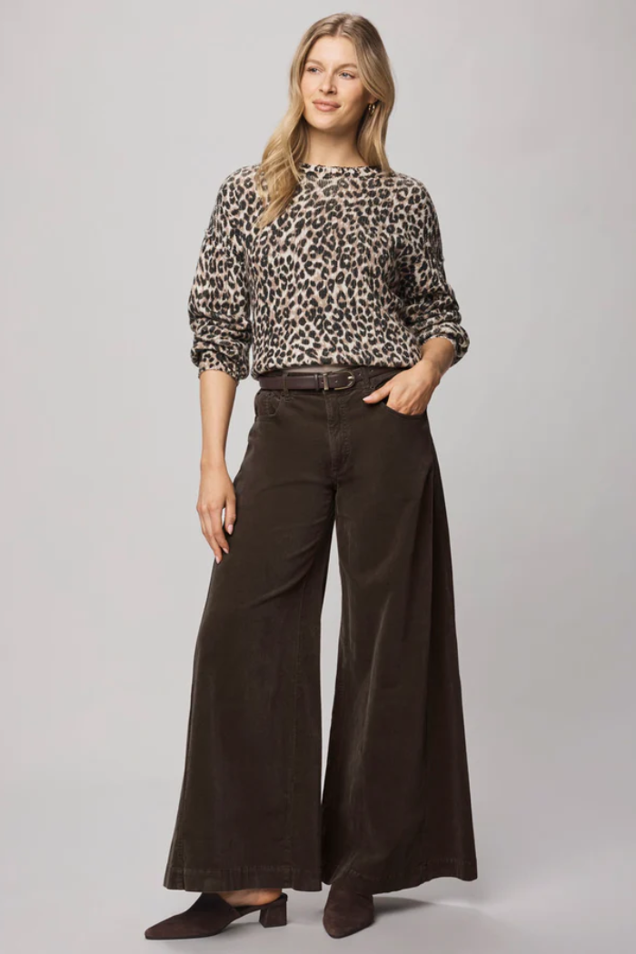 Woman wearing a leopard print top and brown wide-leg pants on a gray background